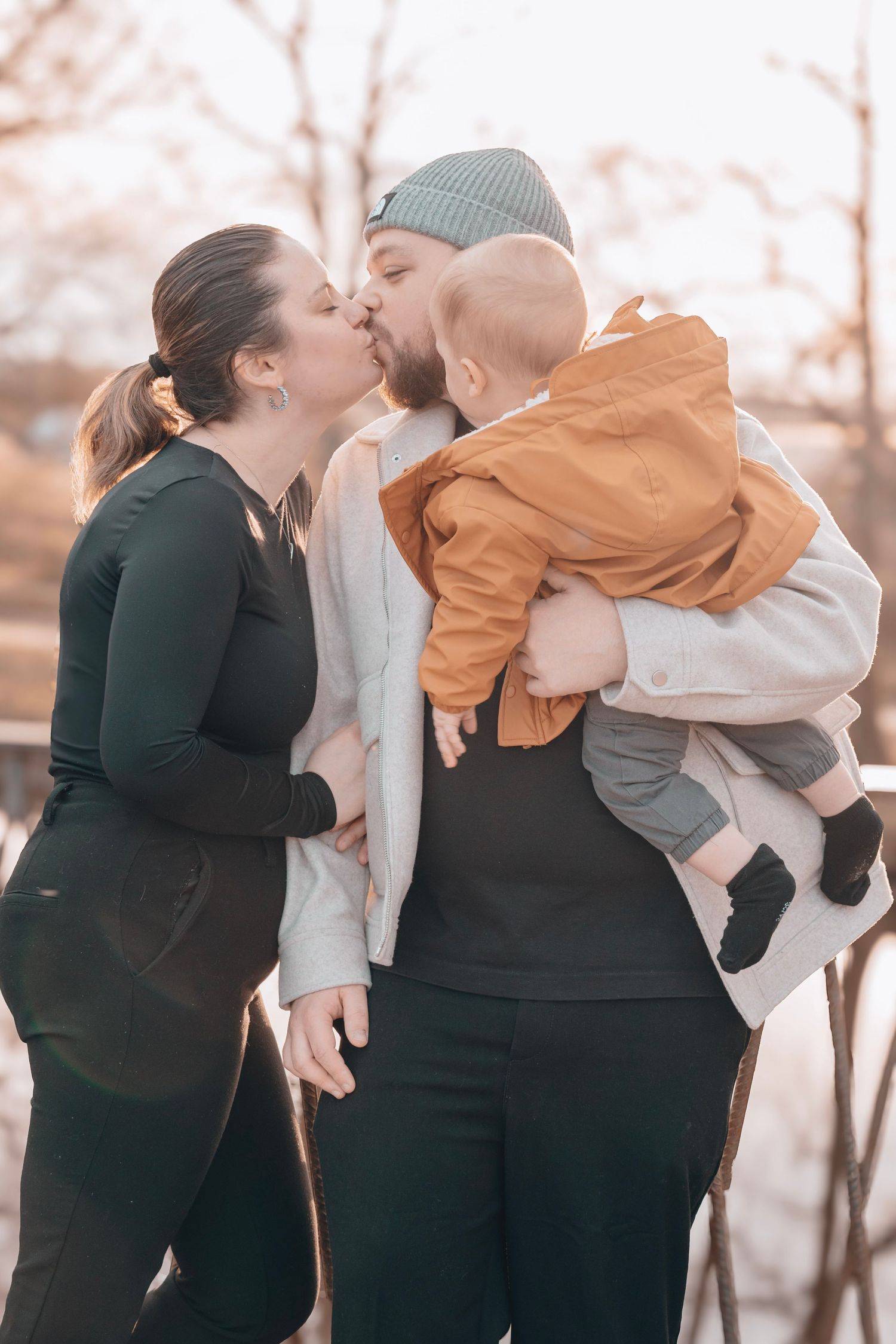 Intimate family moment with toddler in casual winter wear against autumn backdrop.