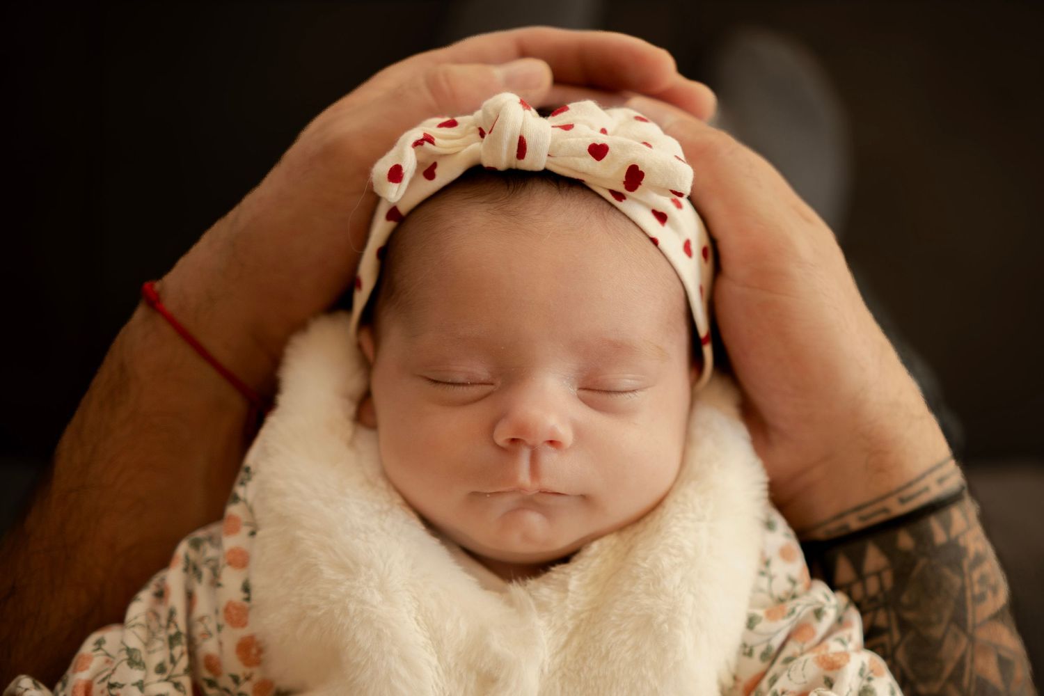 A sleeping newborn baby wearing a polka dot headband rests peacefully in a cozy blanket.
