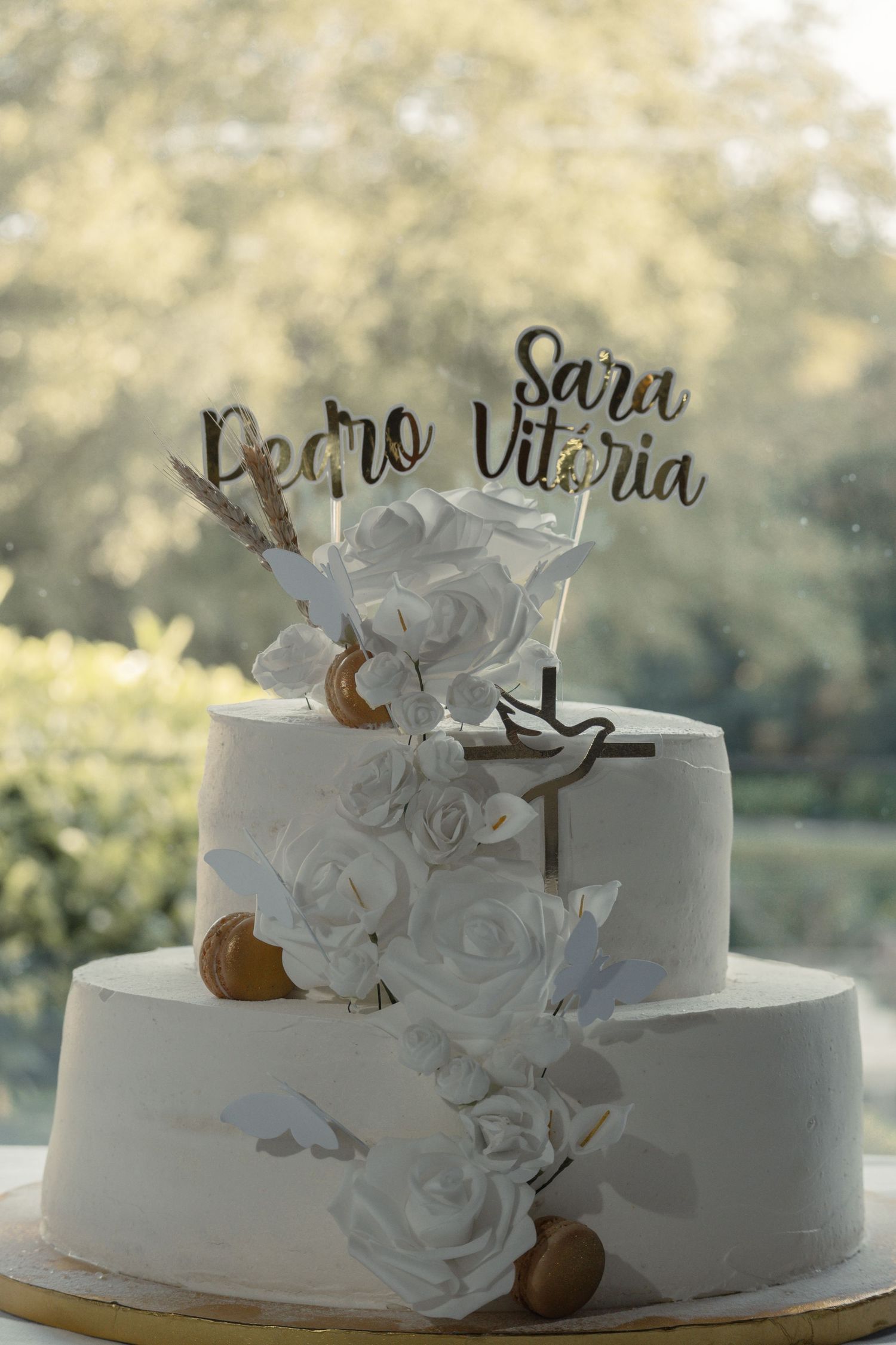 White wedding cake decorated with elegant floral details and custom name text displayed outdoors.