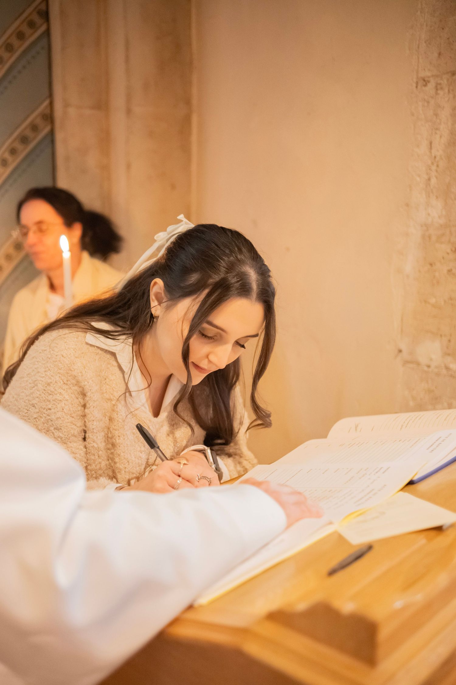 Young woman in beige sweater signing documents at wooden desk in church ceremony.
