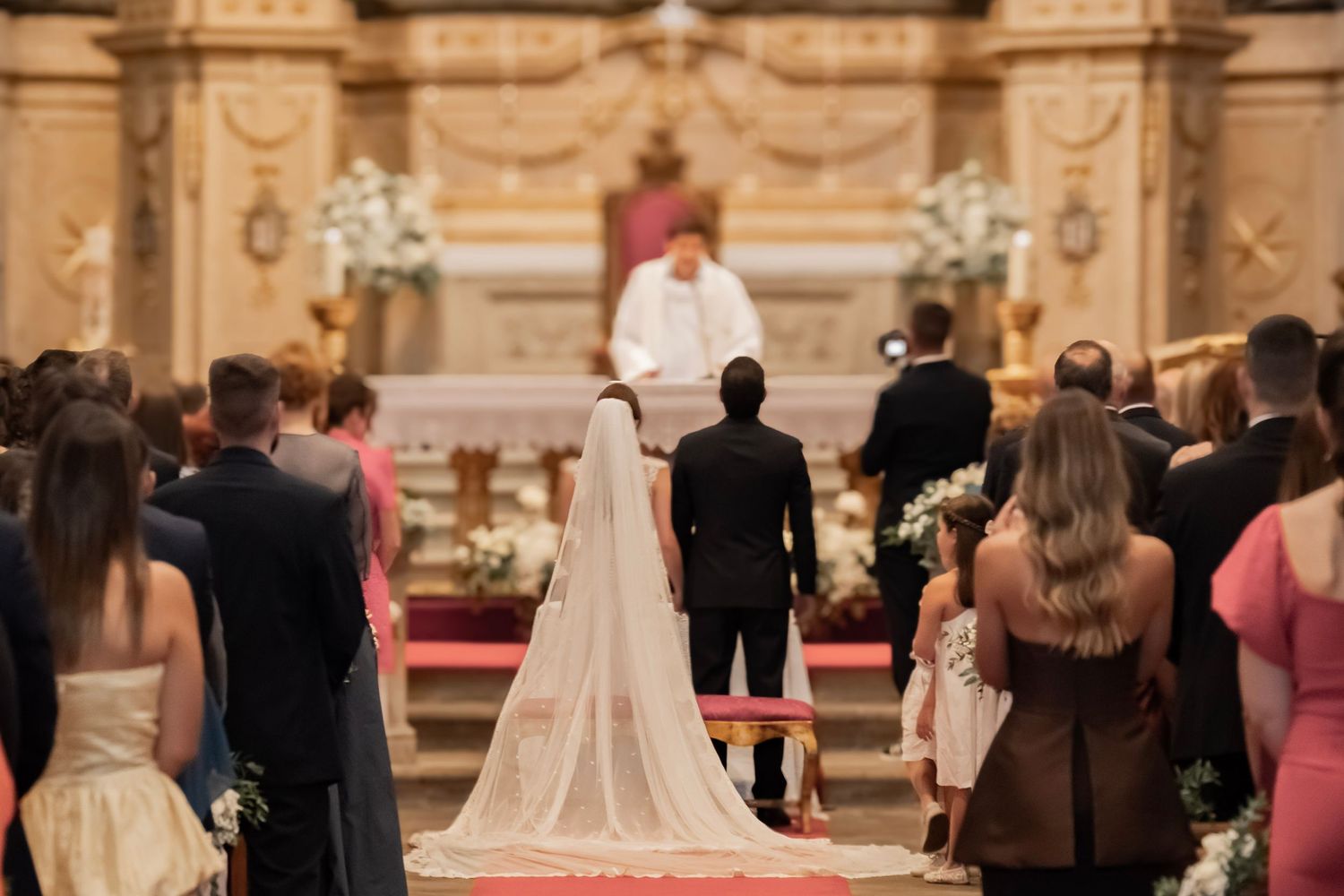 Bride and groom standing at church altar during wedding ceremony with guests seated in ornate cathedral.