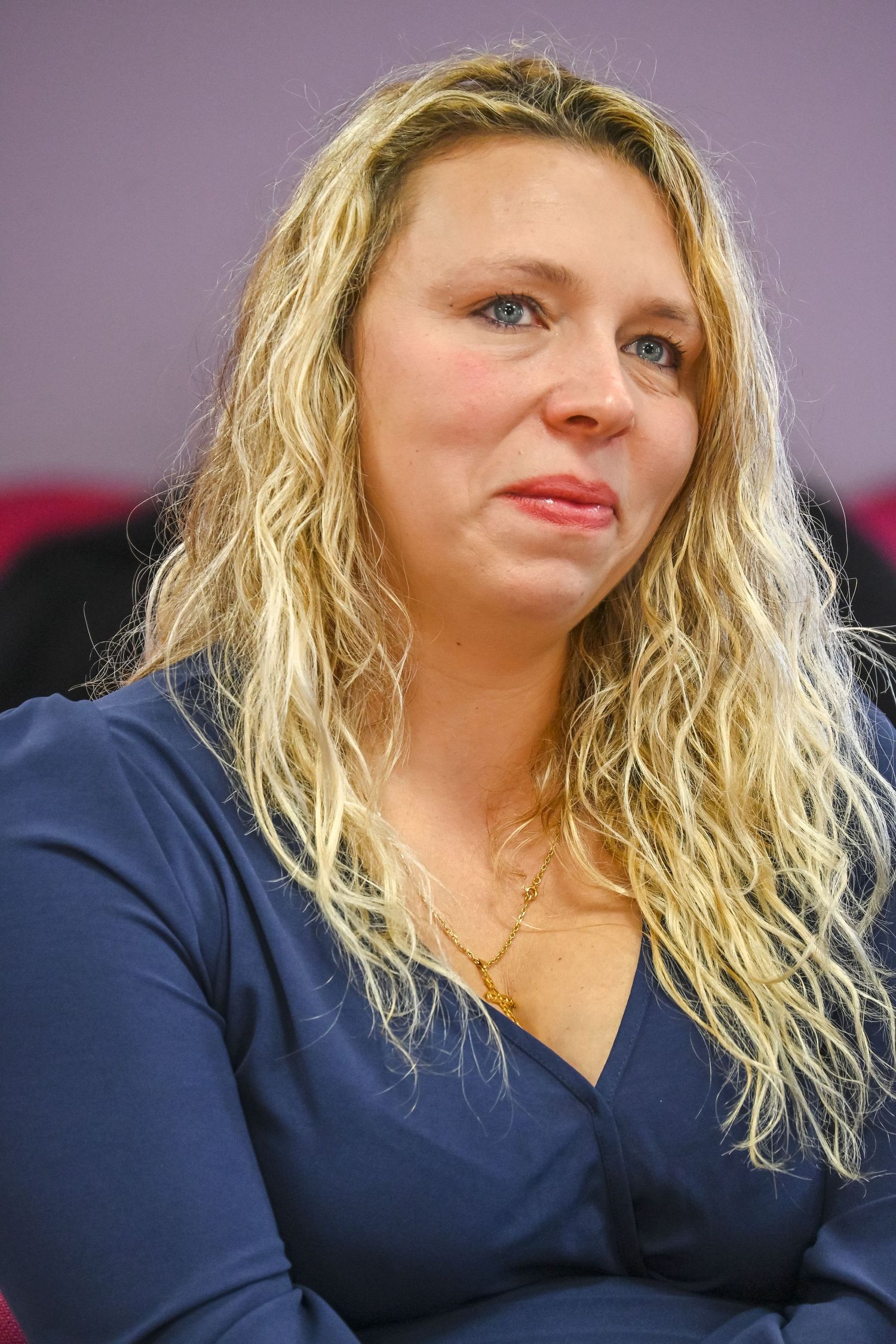 A woman with wavy blonde hair and navy blouse in an office setting.