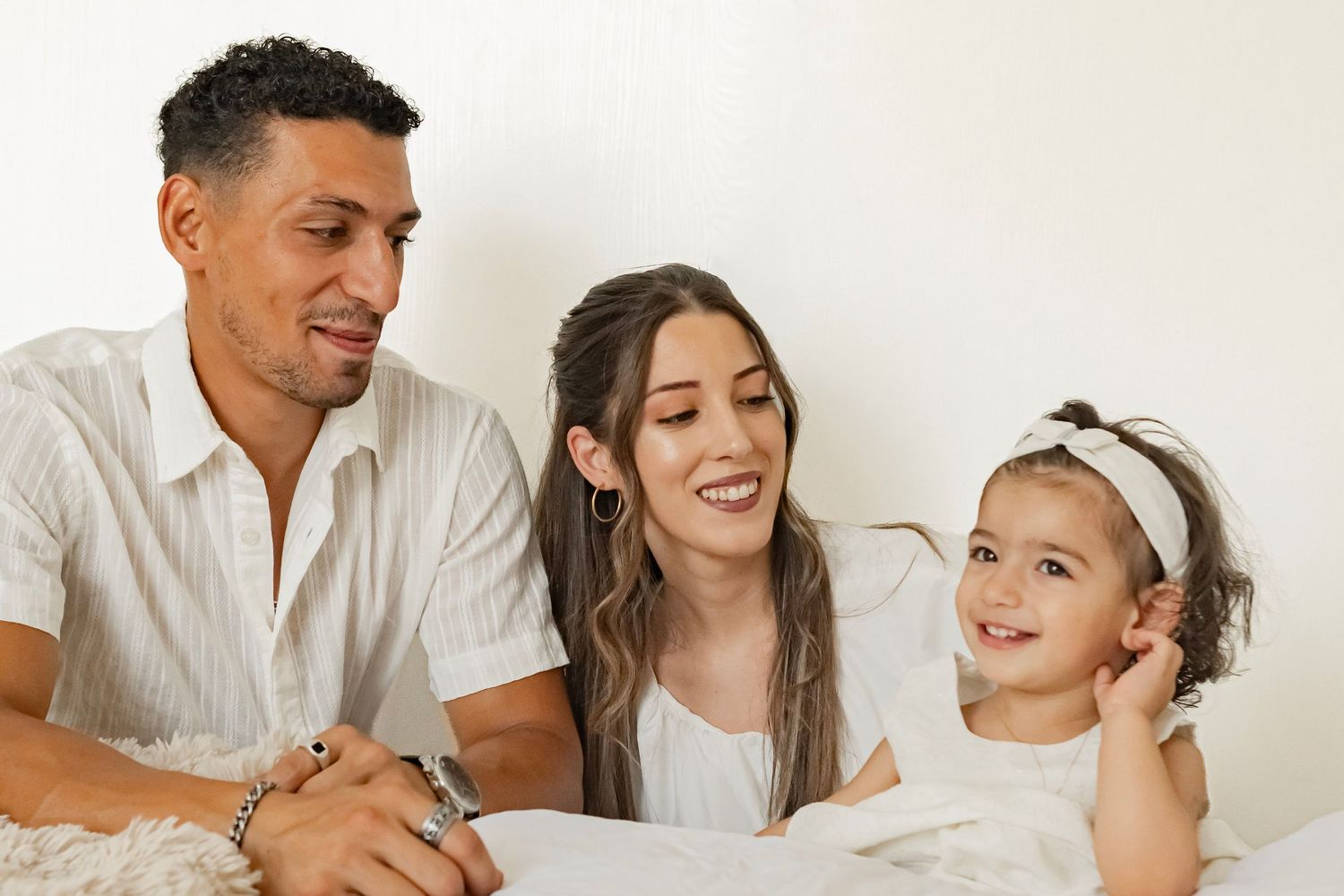 Happy family portrait with parents and toddler daughter smiling together against white background.
