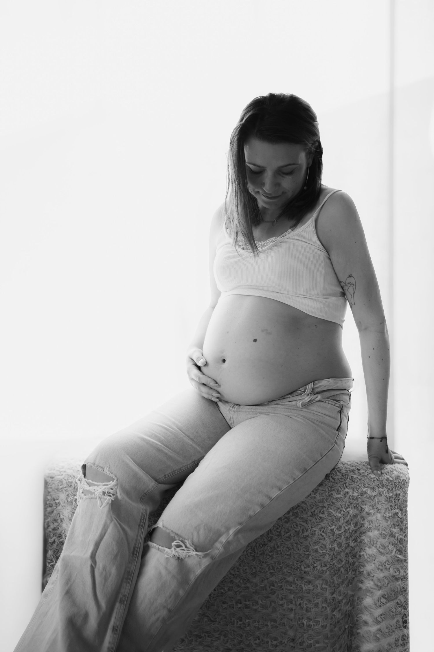 Black and white artistic maternity photos showing a pregnant woman in casual attire resting on patterned furniture.