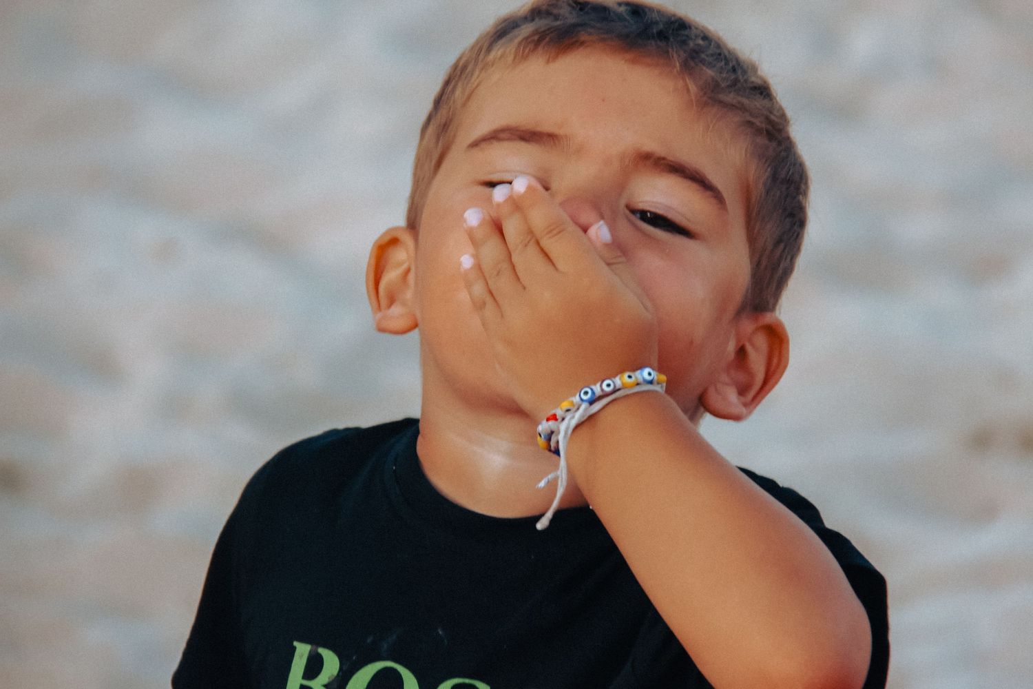 A young child in a black shirt covers their face with their hand in the sunlight.