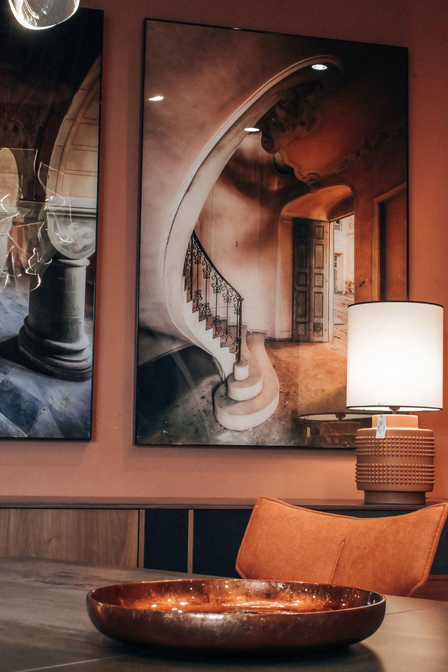 Modern interior design with orange walls featuring spiral staircase artwork, table lamp and copper decorative bowl.