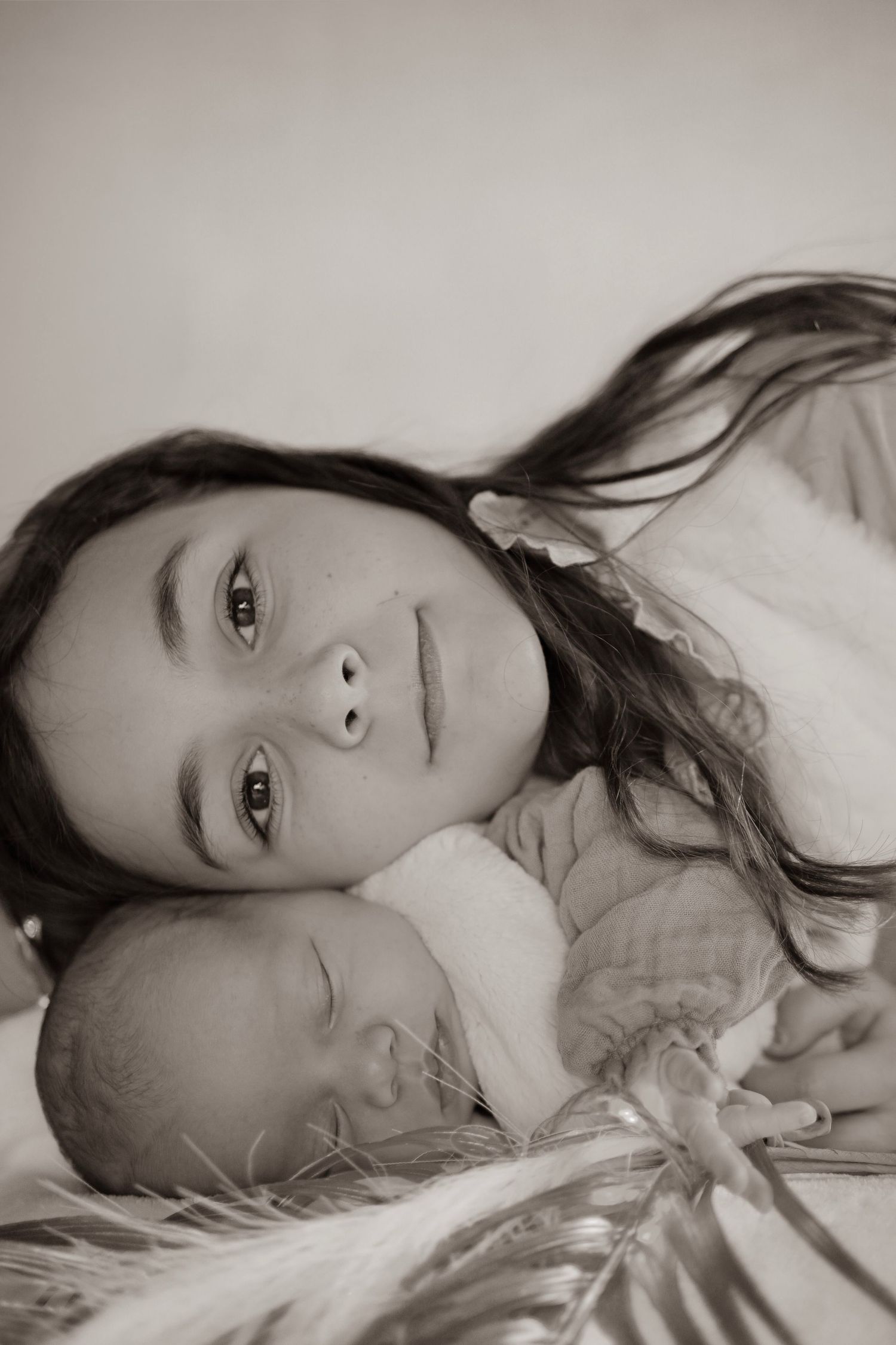 A series of black and white portraits showing someone reclining on white bedding with long dark hair.