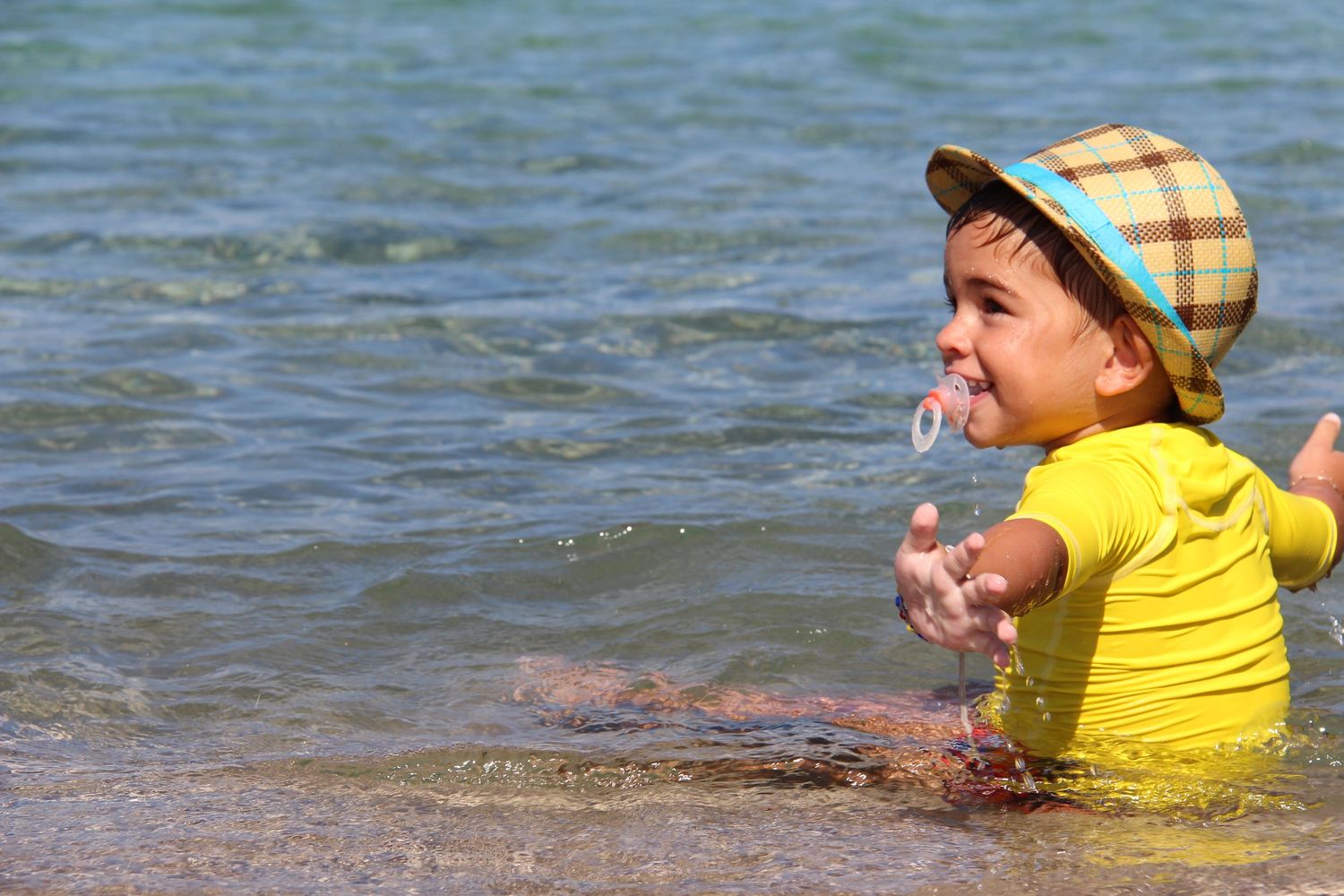 A person in a bright yellow shirt plays in clear blue water, splashing and creating a playful sequence of movements.