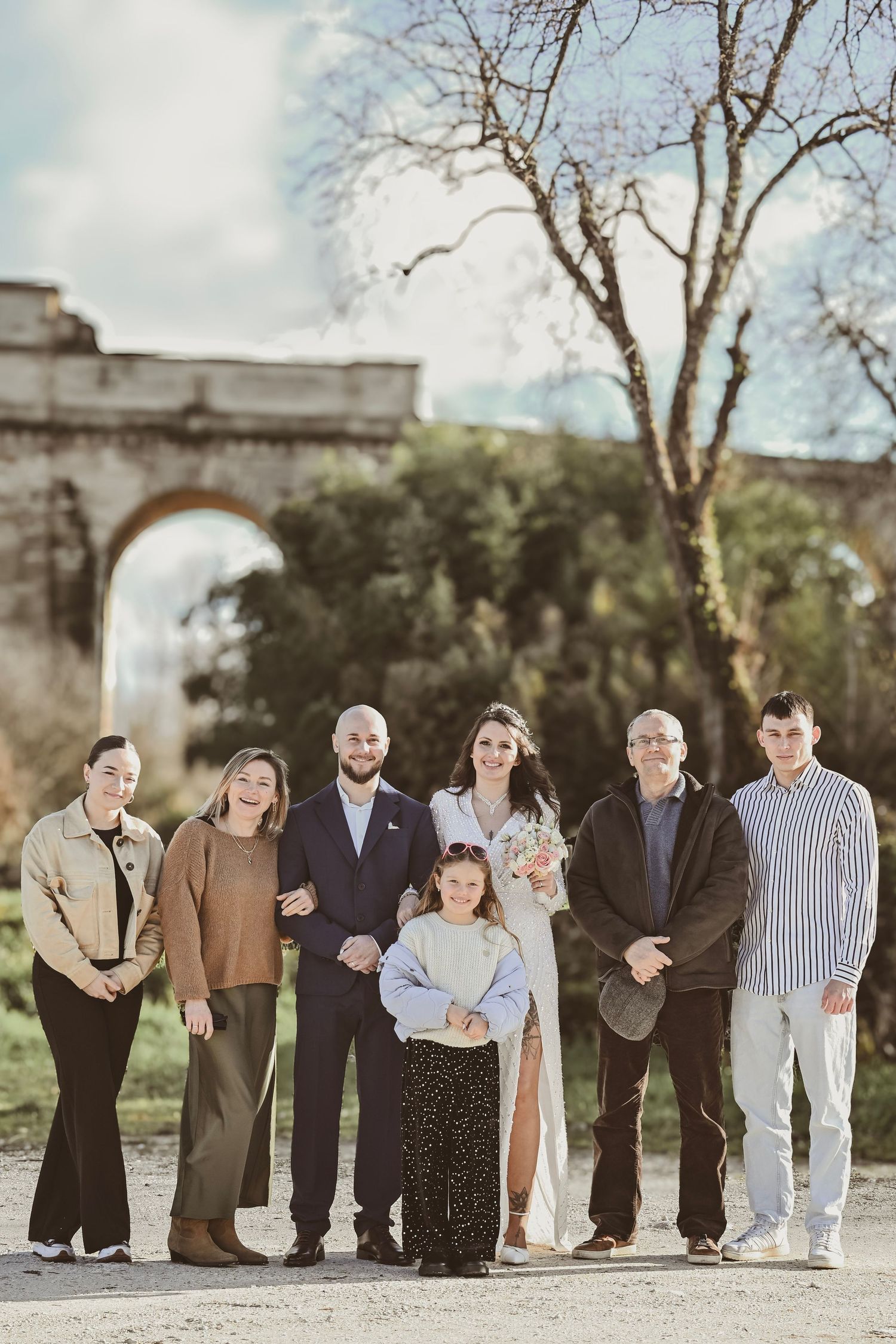 Extended family gathers for a formal portrait in front of historic stone arch bridge.