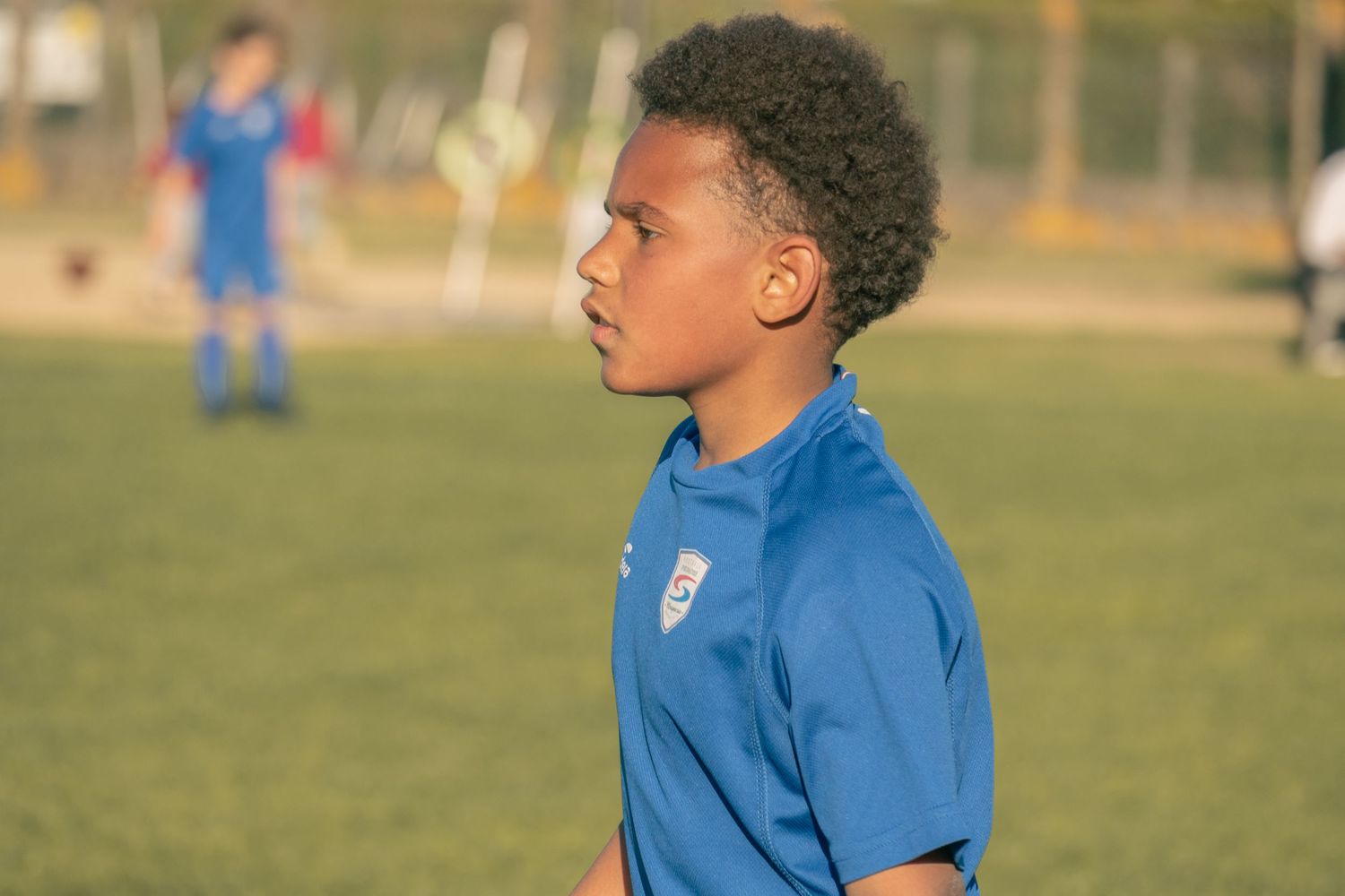 Young athlete in blue soccer uniform stands focused on soccer field during training session.
