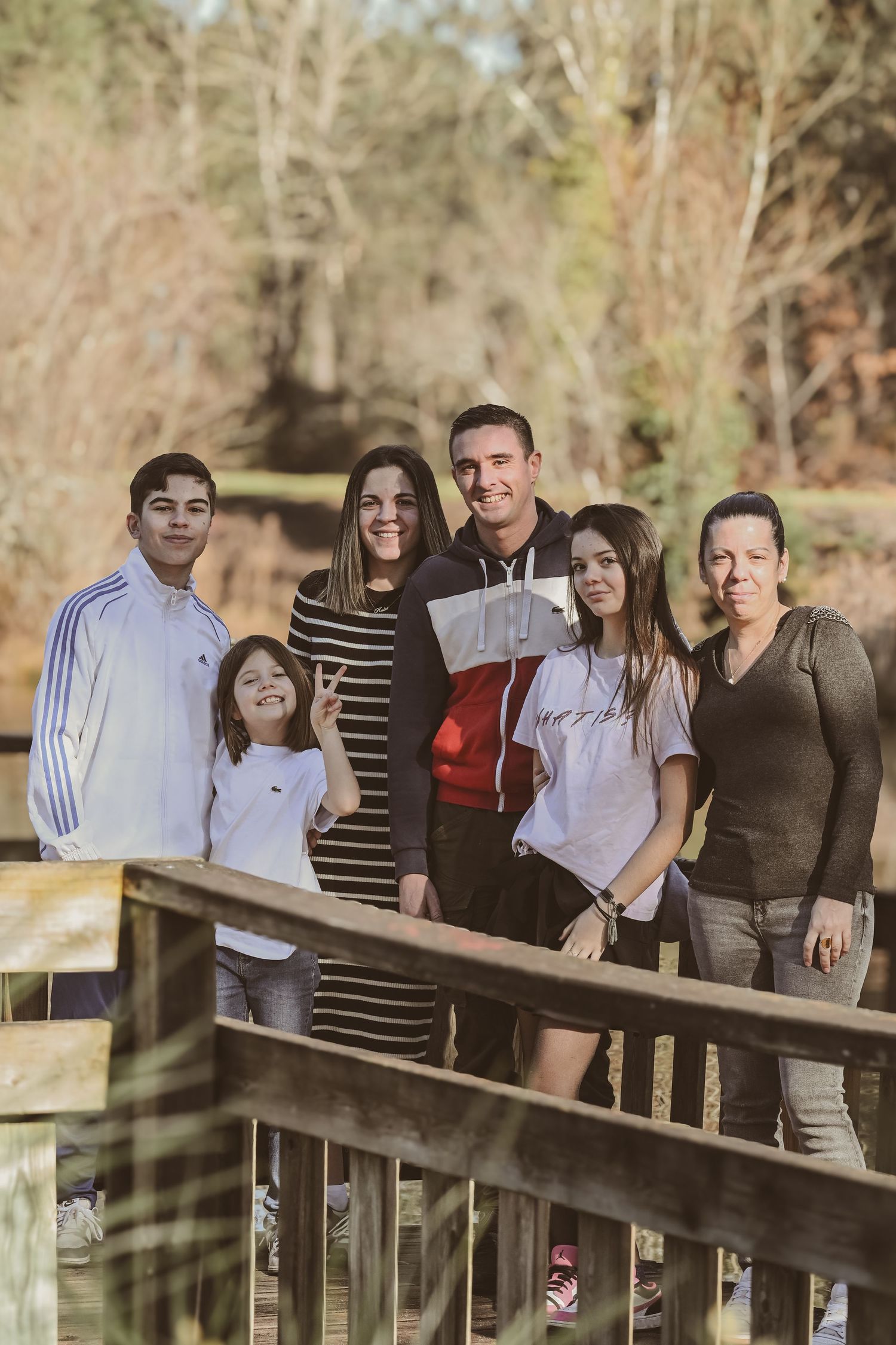 Family group stands together on a wooden bridge in a natural setting.