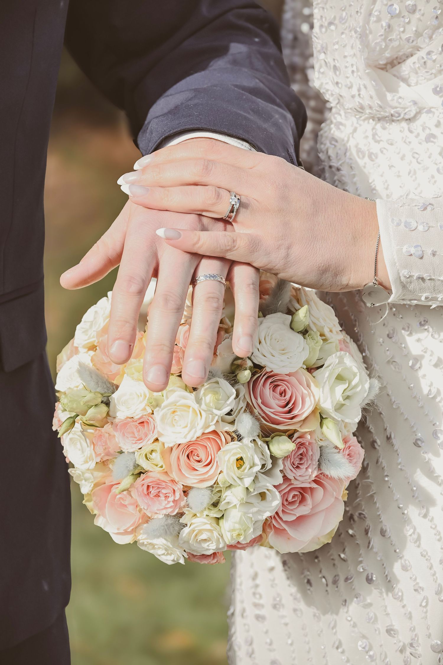 Wedding rings displayed on hands over bouquet of pink and white roses.