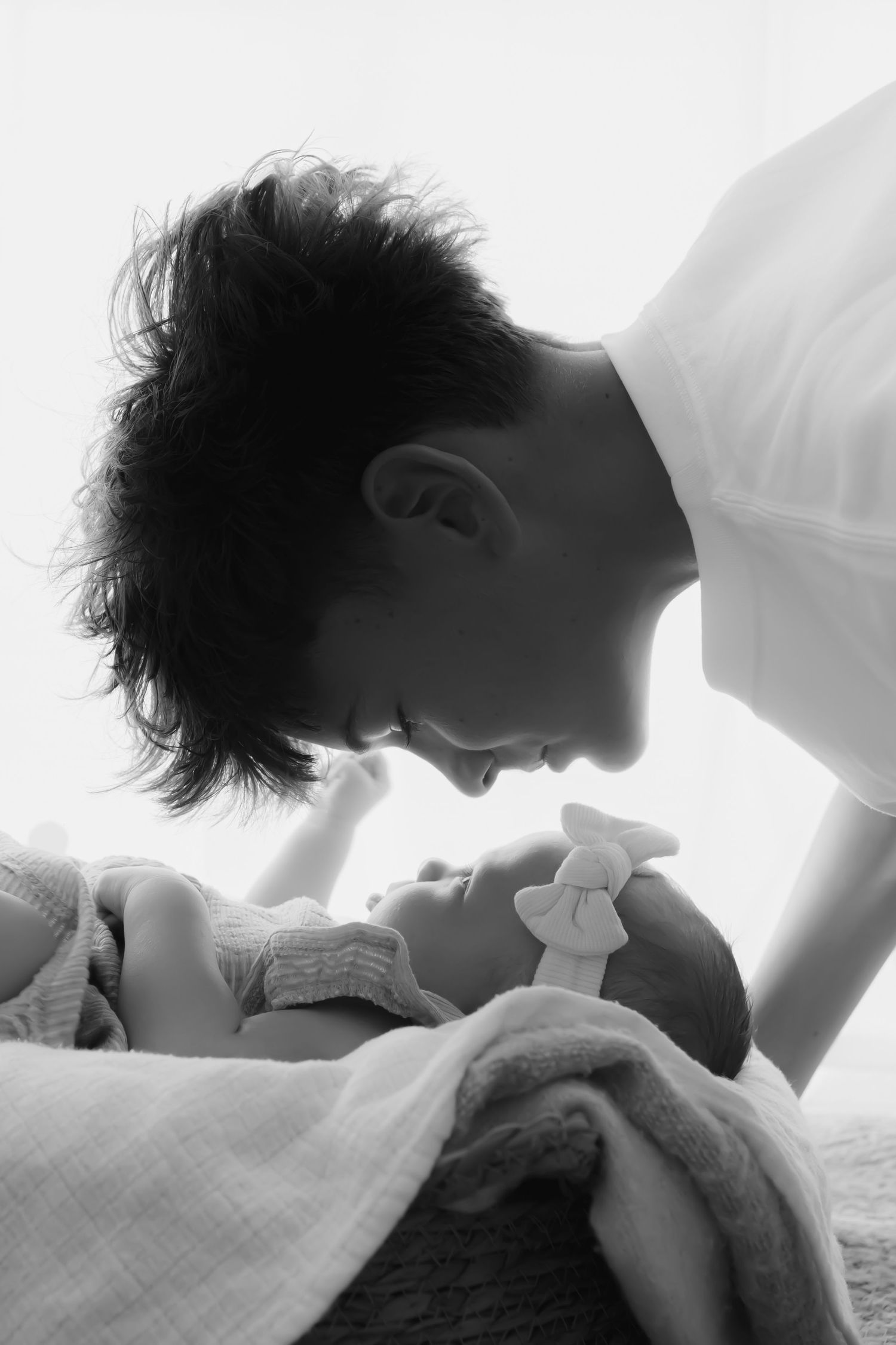 Black and white photo of a young mother leaning over her newborn baby, sharing a tender moment.