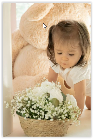 A small child in white leans over to look at a basket filled with baby's breath flowers and white roses.
