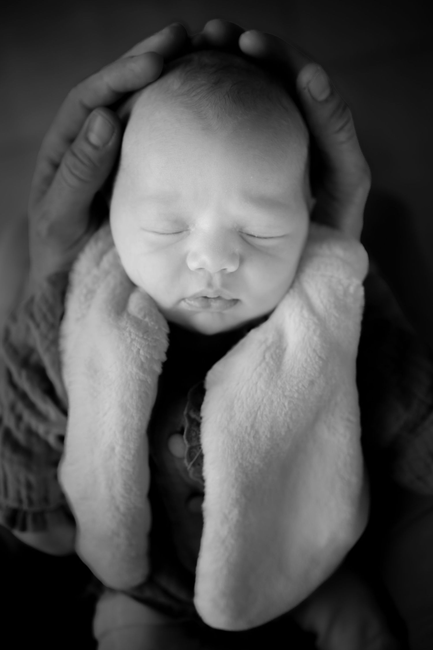 A black and white photo series showing a sleeping newborn baby in gentle hands against a dark background.