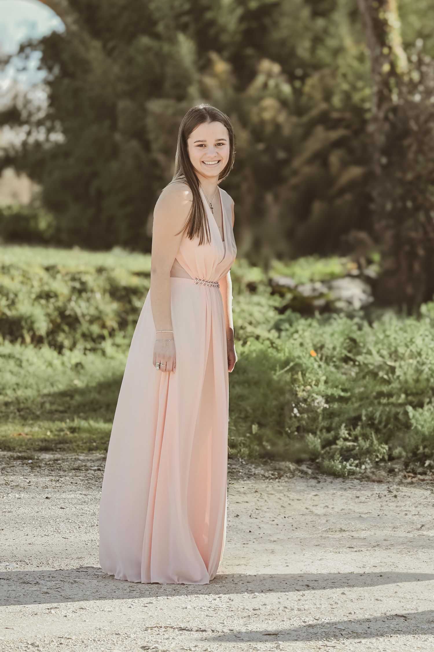 A woman in a flowing peach-colored maxi dress poses outdoors in natural lighting.
