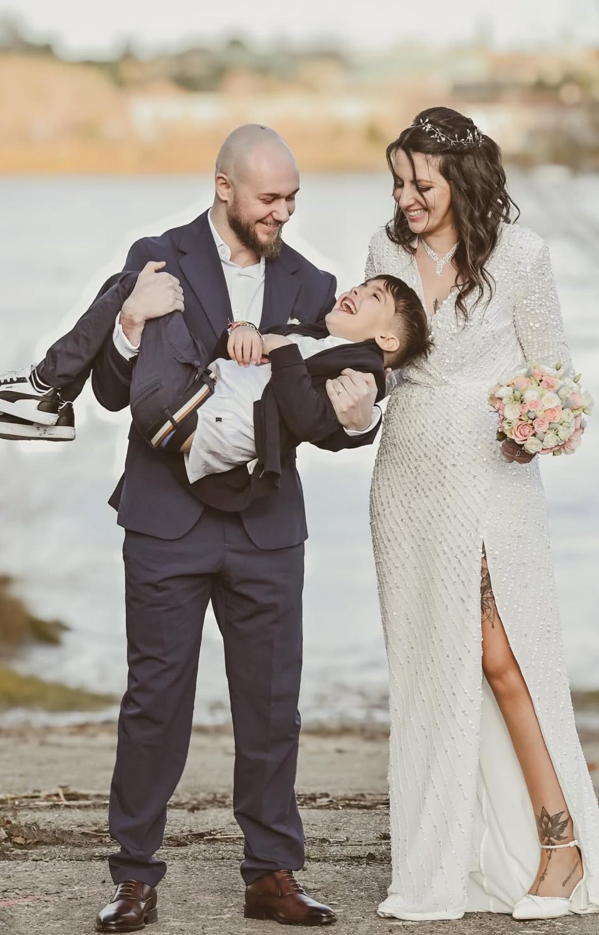 A couple in wedding attire shares a playful moment on a beach, with the groom dipping the bride in an elegant pose.