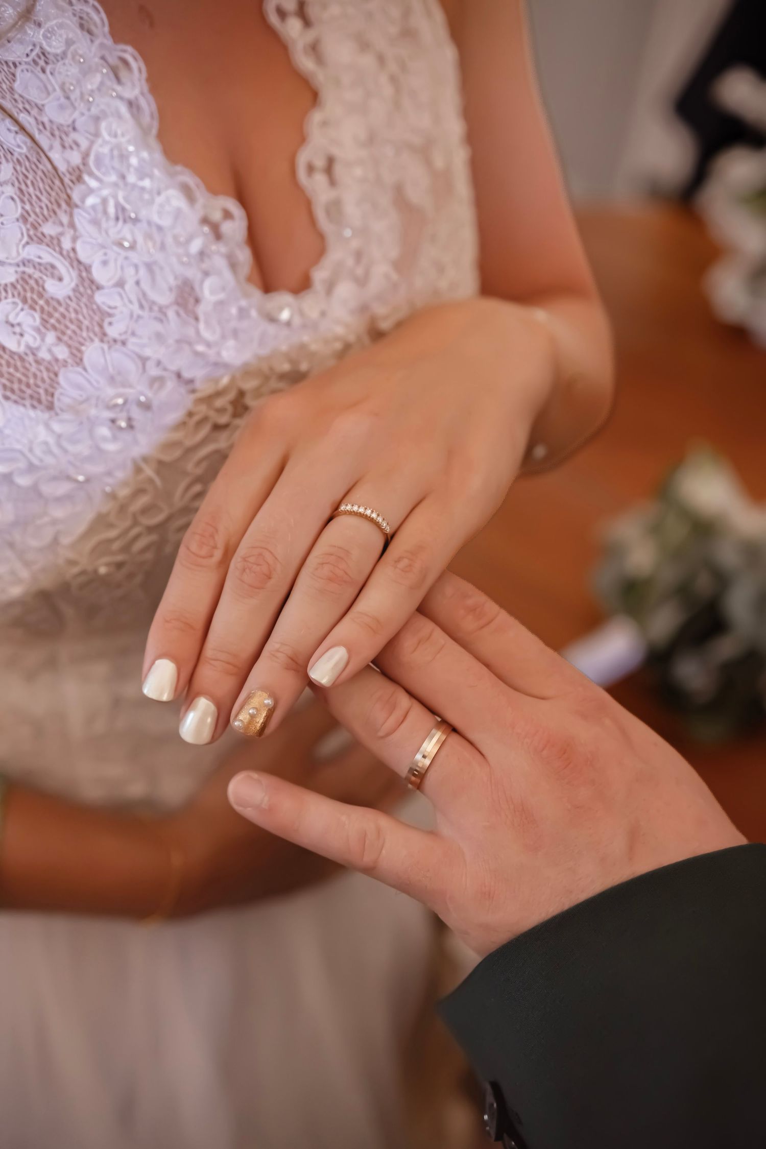 Bride and groom exchanging gold wedding rings, bride wearing lace dress with white manicure.