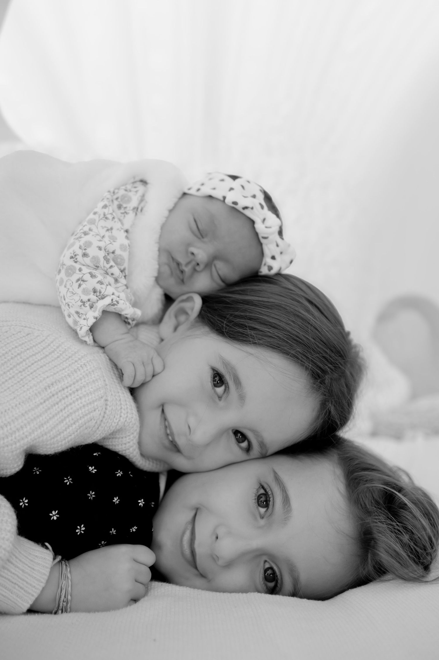 A heartwarming black and white portrait showing three people laying together in a tender embrace.