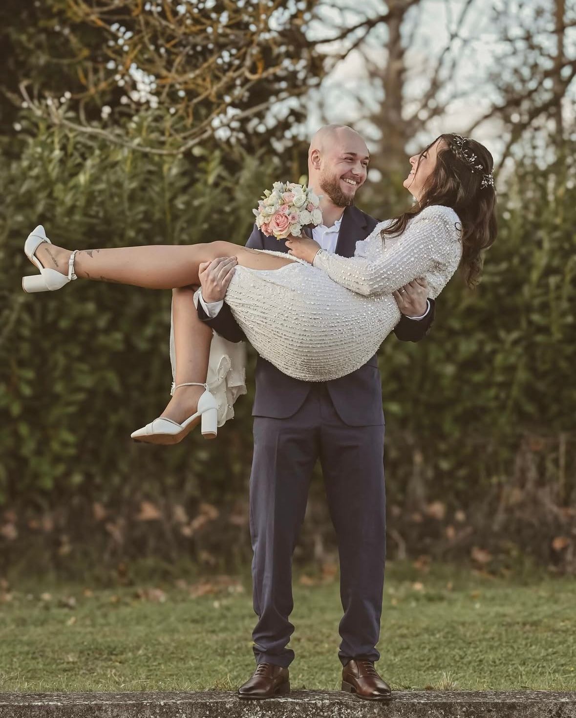 A couple twirls together in a romantic dance pose outdoors on grassy lawn with autumn trees in background.