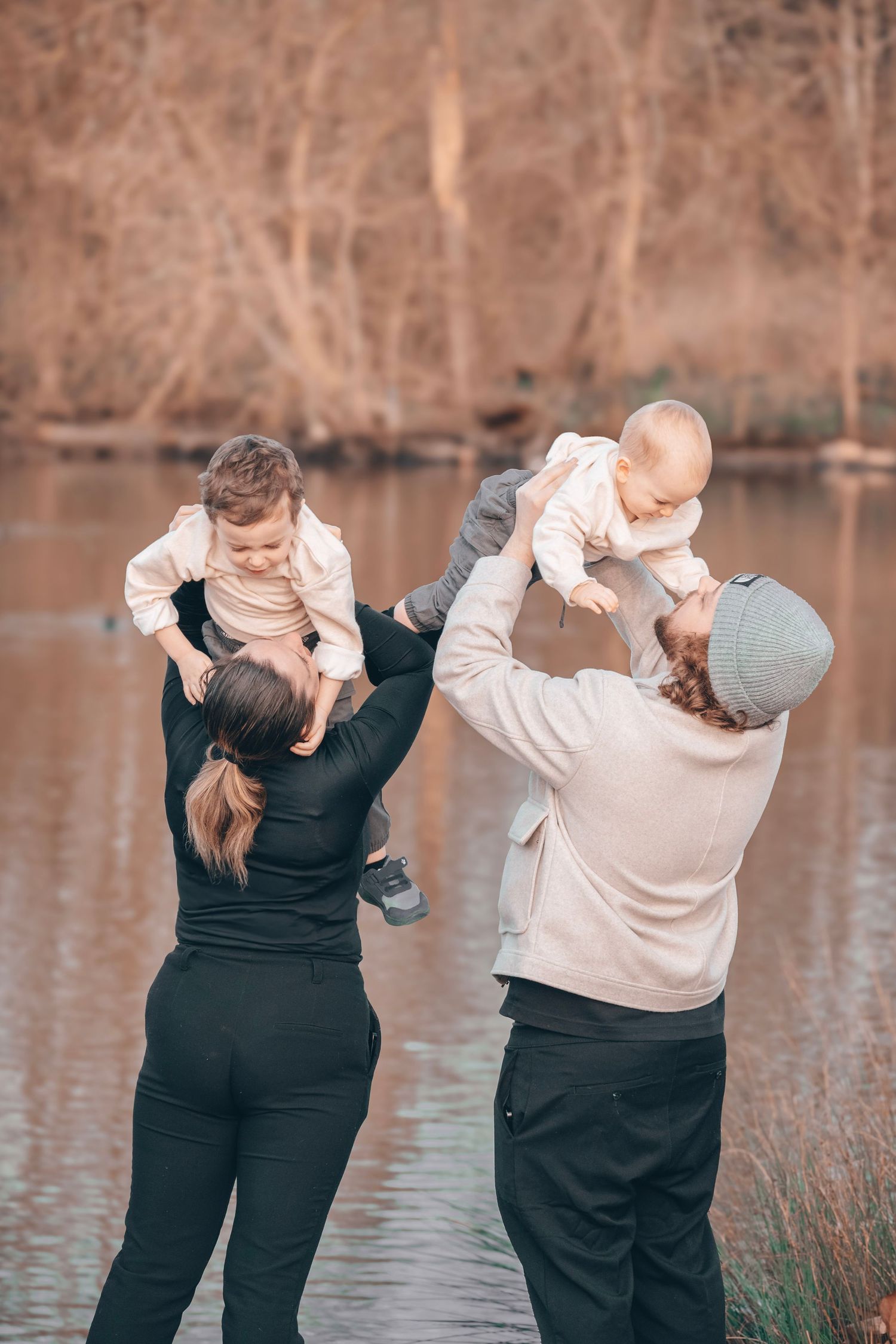 Parents playfully lift their young children by the water's edge.