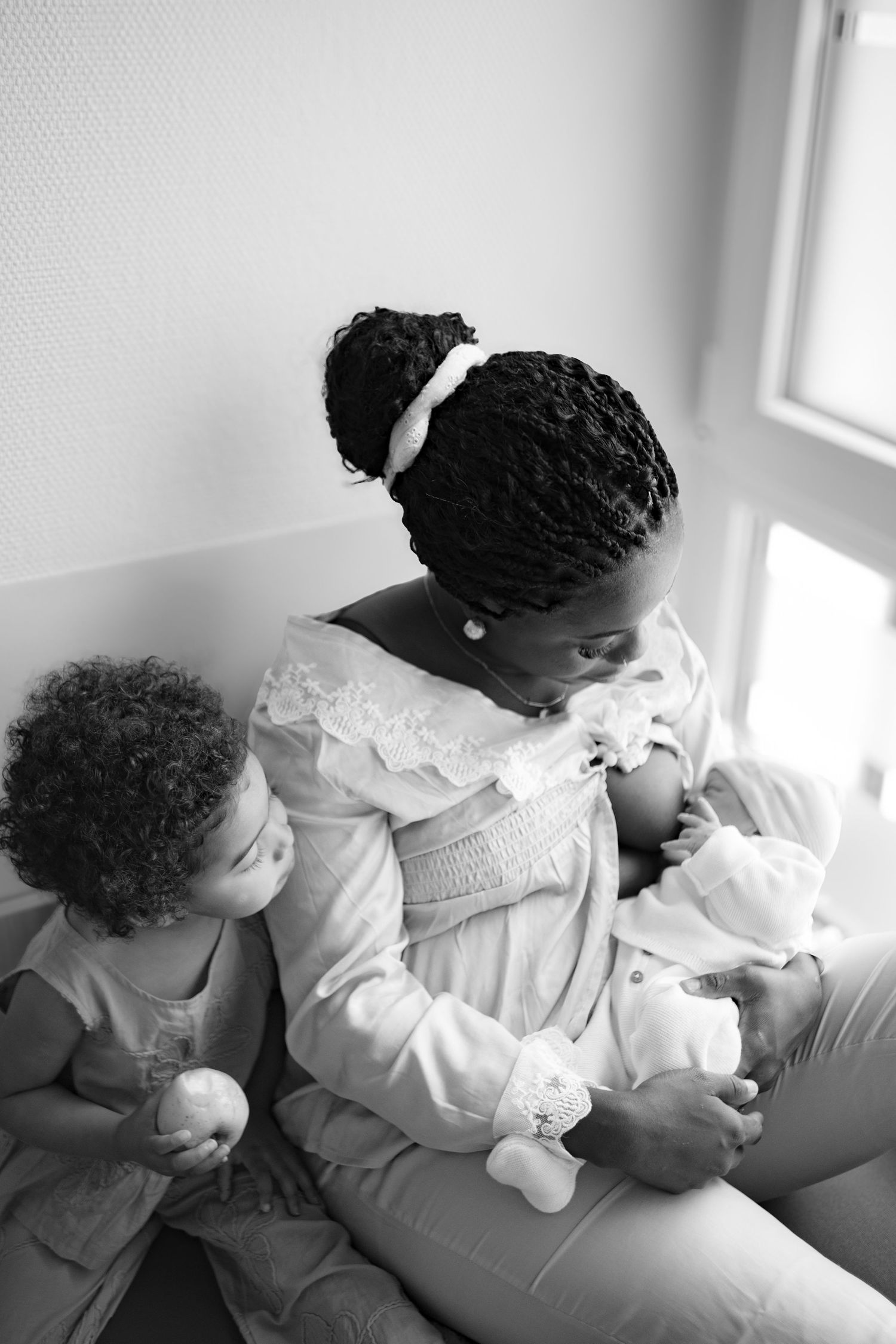 Black and white photo of a mother breastfeeding her newborn while her toddler sits beside her.