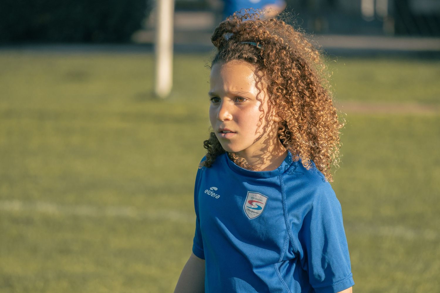 Soccer player in blue jersey with curly hair on outdoor field during practice session.