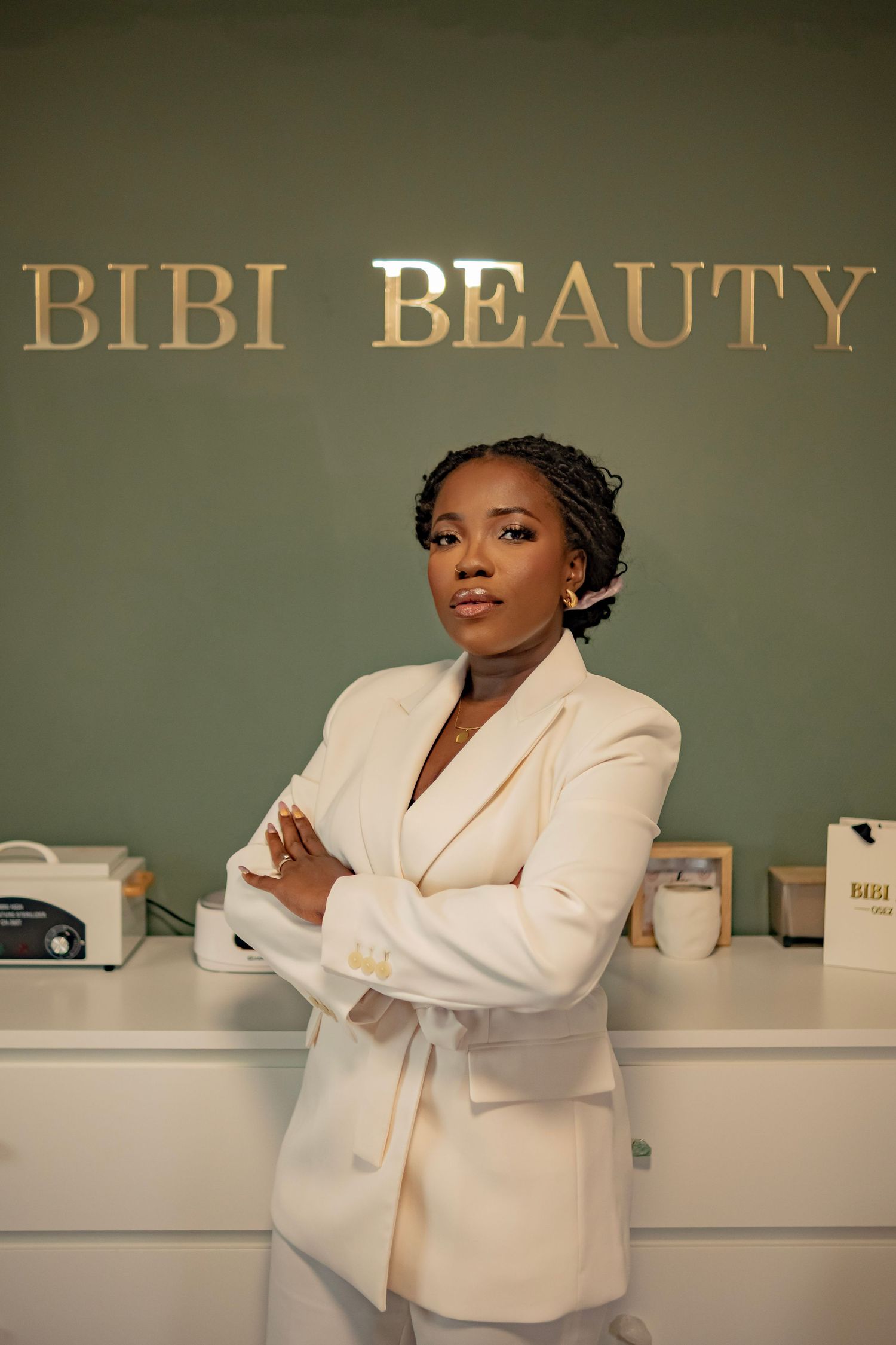 A confident Black woman in a white blazer stands arms crossed before the Bibi Beauty salon sign.