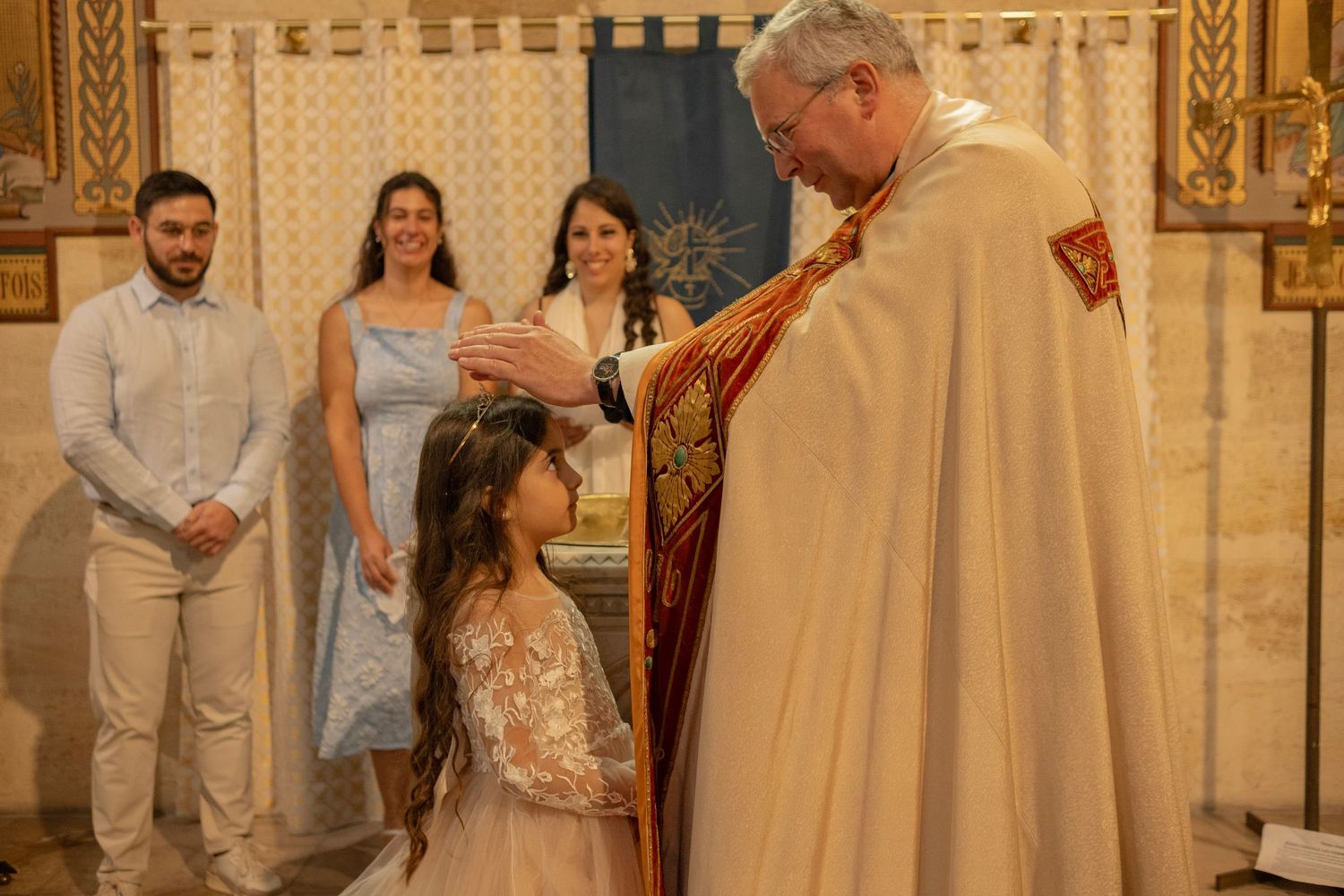 Priest placing hand on young girl's head during a religious ceremony in an ornate church.
