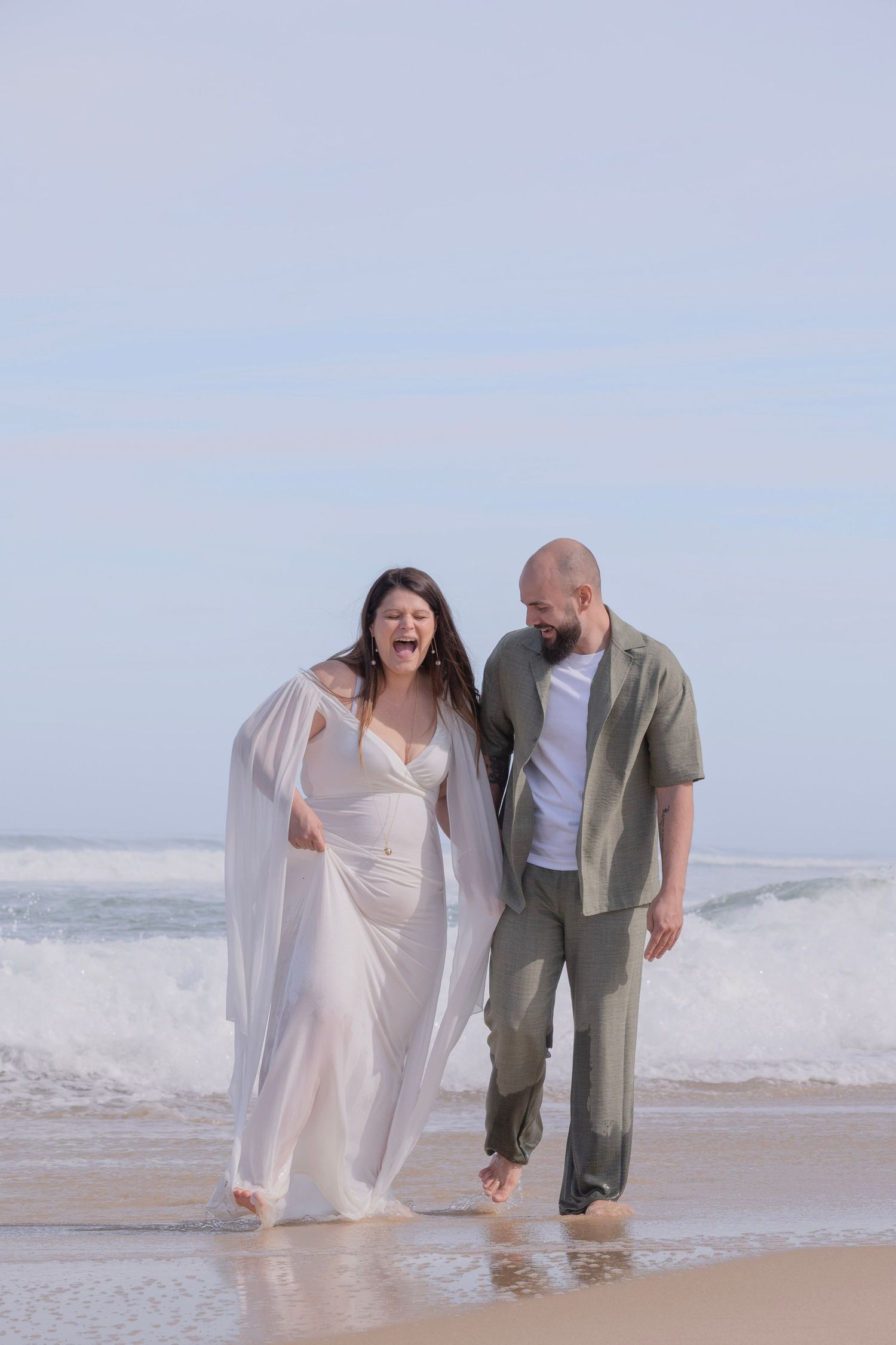 A couple walking together on a sandy beach with waves crashing behind them in dreamy light.