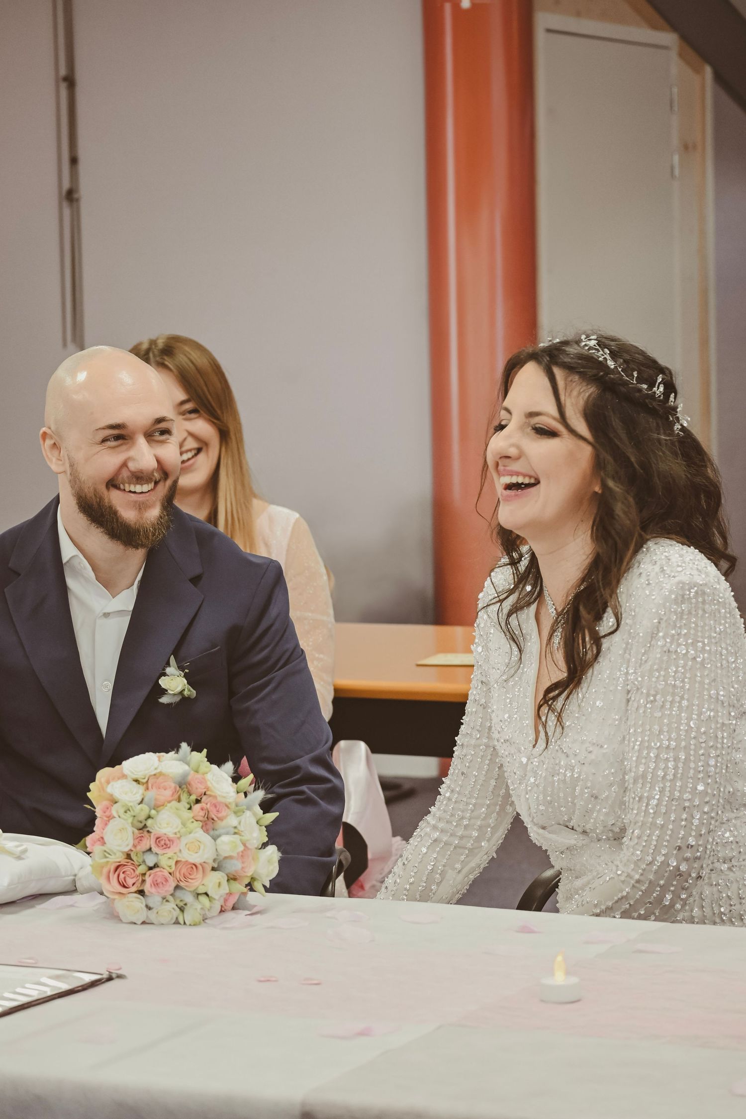 A joyful wedding celebration scene with laughter and a pink floral bouquet on the table.