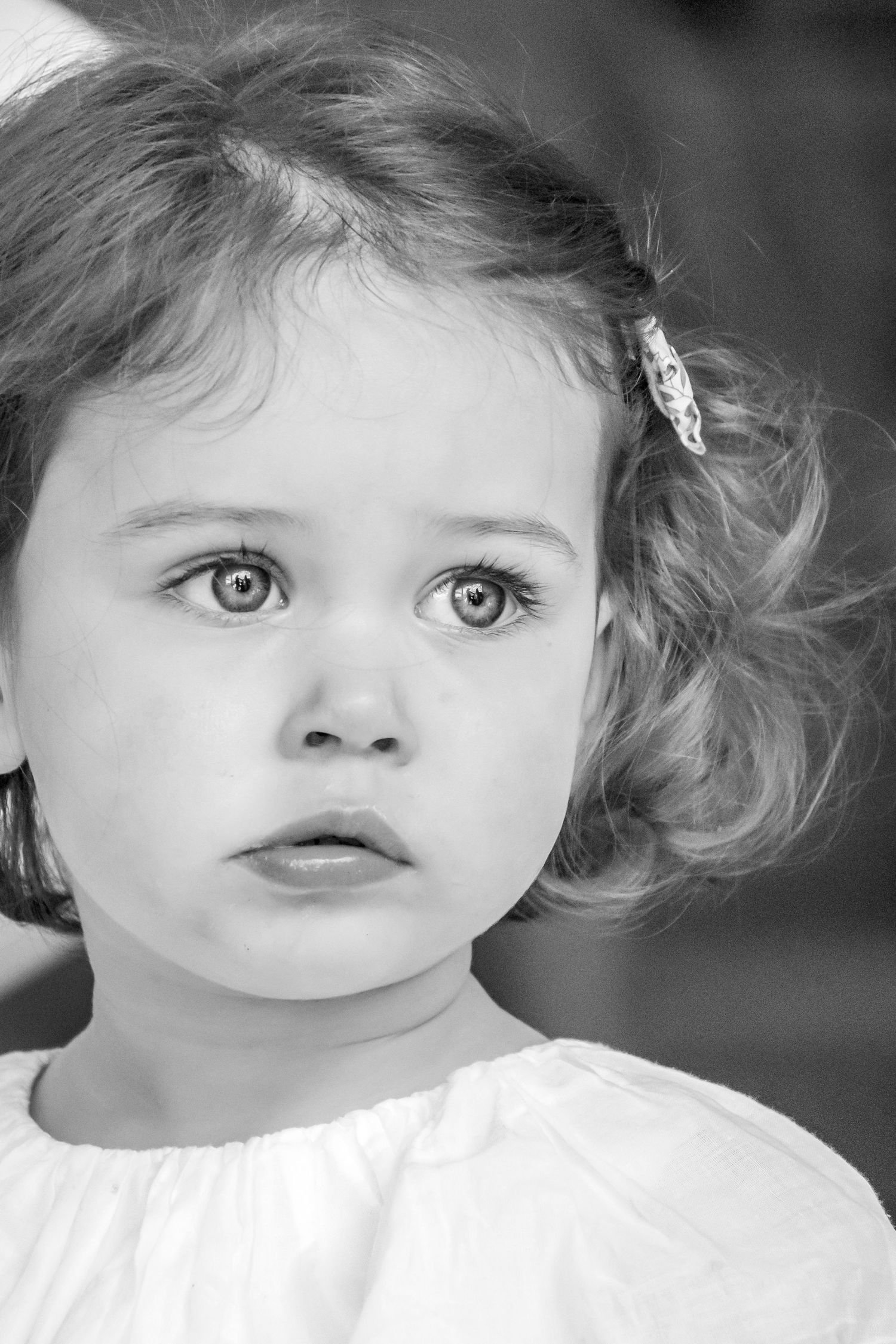 Black and white portrait of a young girl with curly hair and big expressive eyes wearing a white dress.