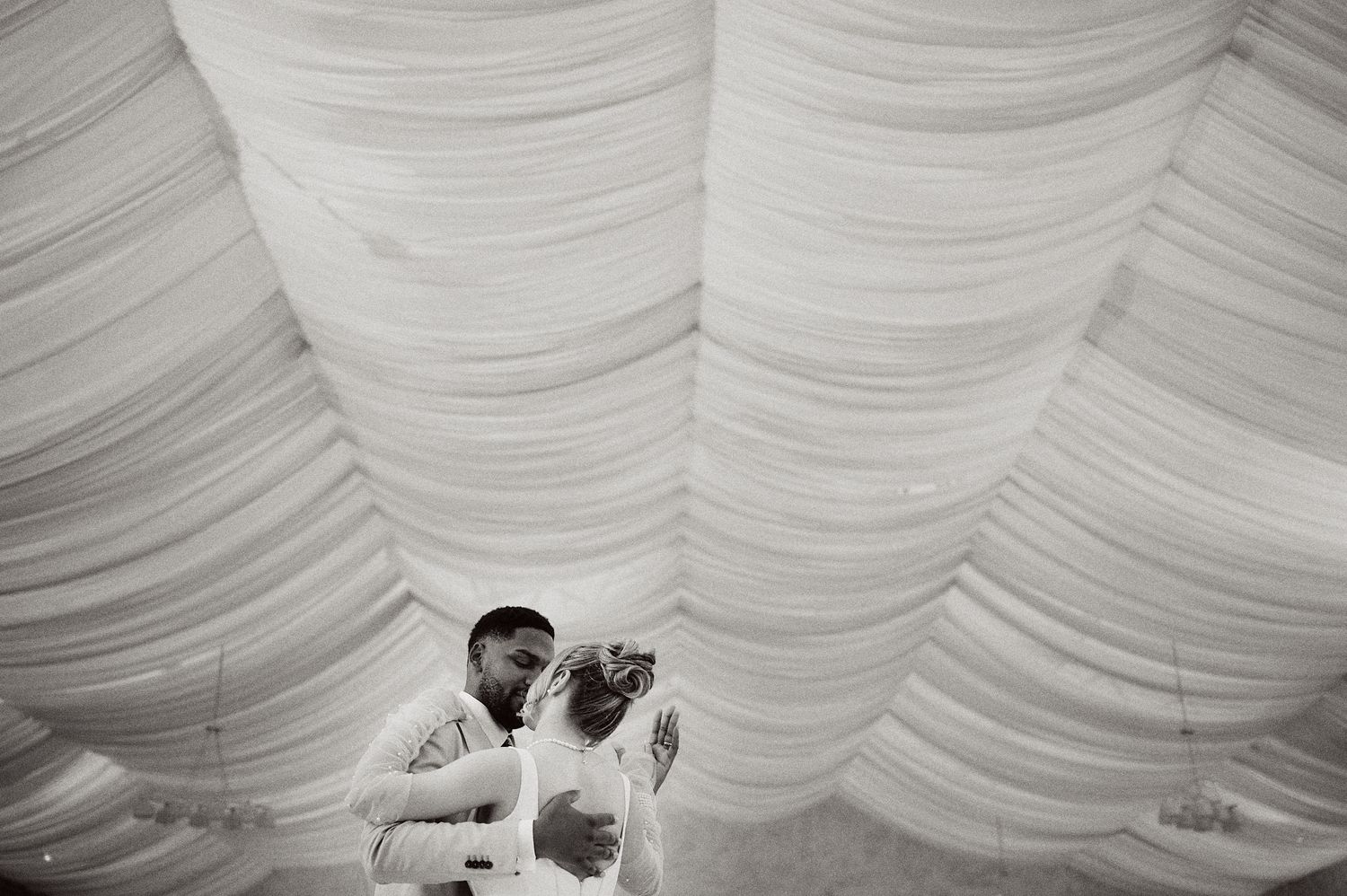 Wedding couple shares an intimate moment under draped white fabric at their reception venue.