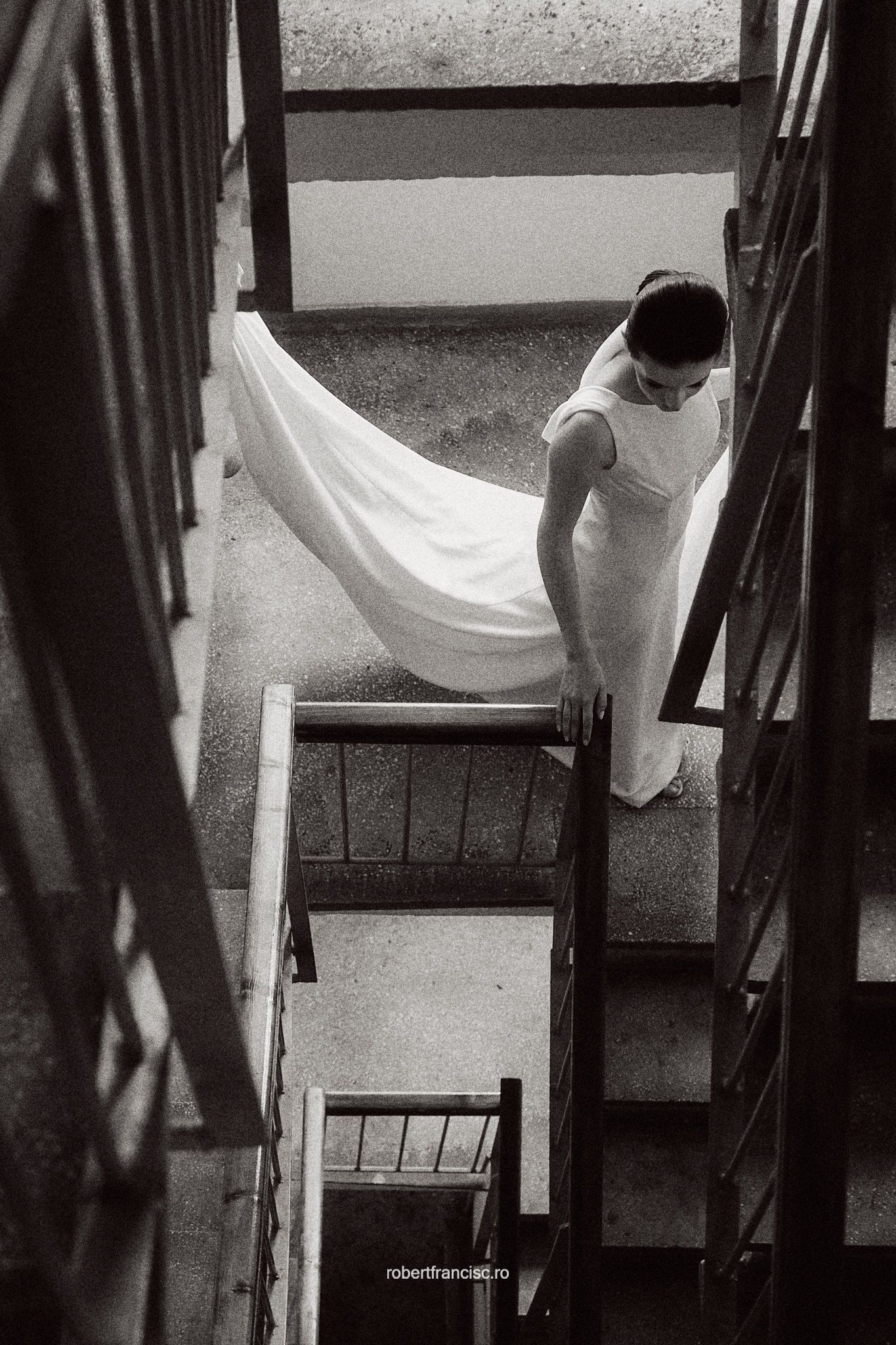 A dramatic black and white photo captures a flowing white dress on a spiral staircase.
