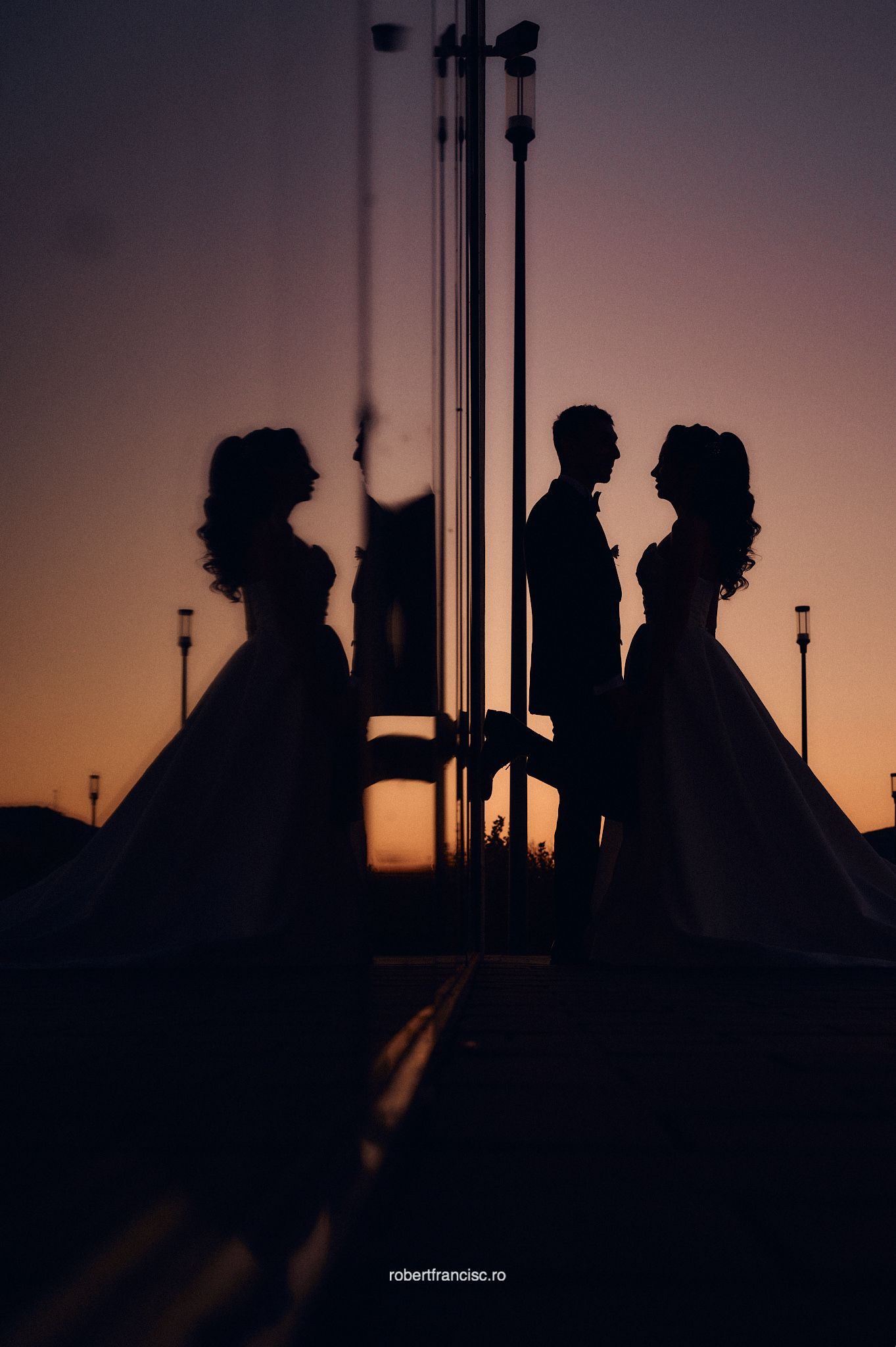Silhouettes of couples in elegant dresses stand against a sunset sky with dramatic lighting and reflective surfaces.