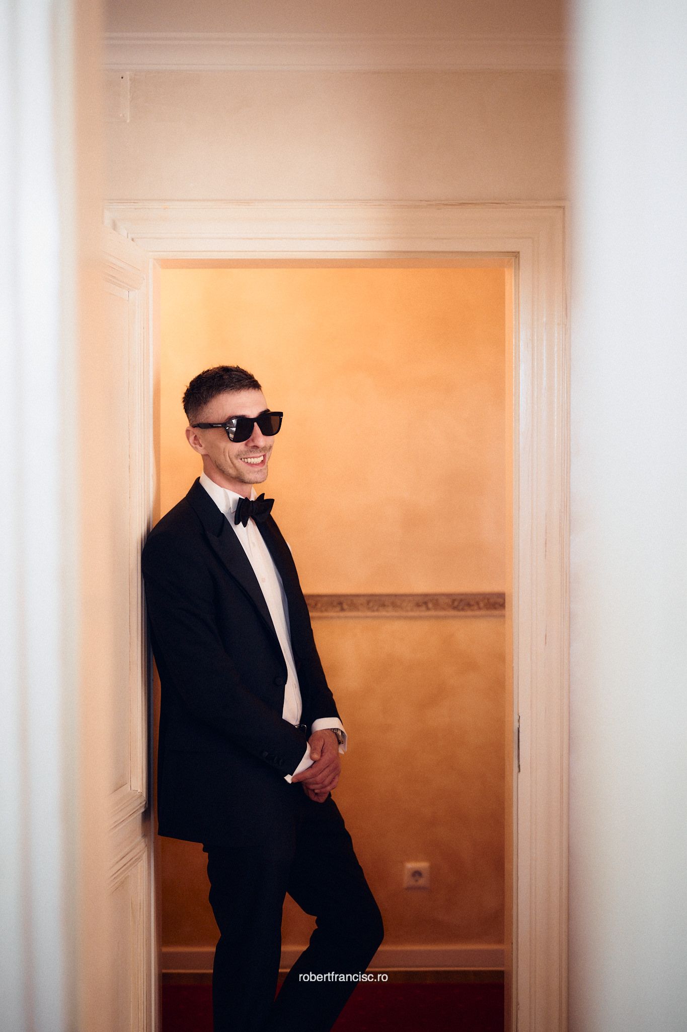 Three connected photos show someone in a black suit and sunglasses walking through a warmly lit hallway.