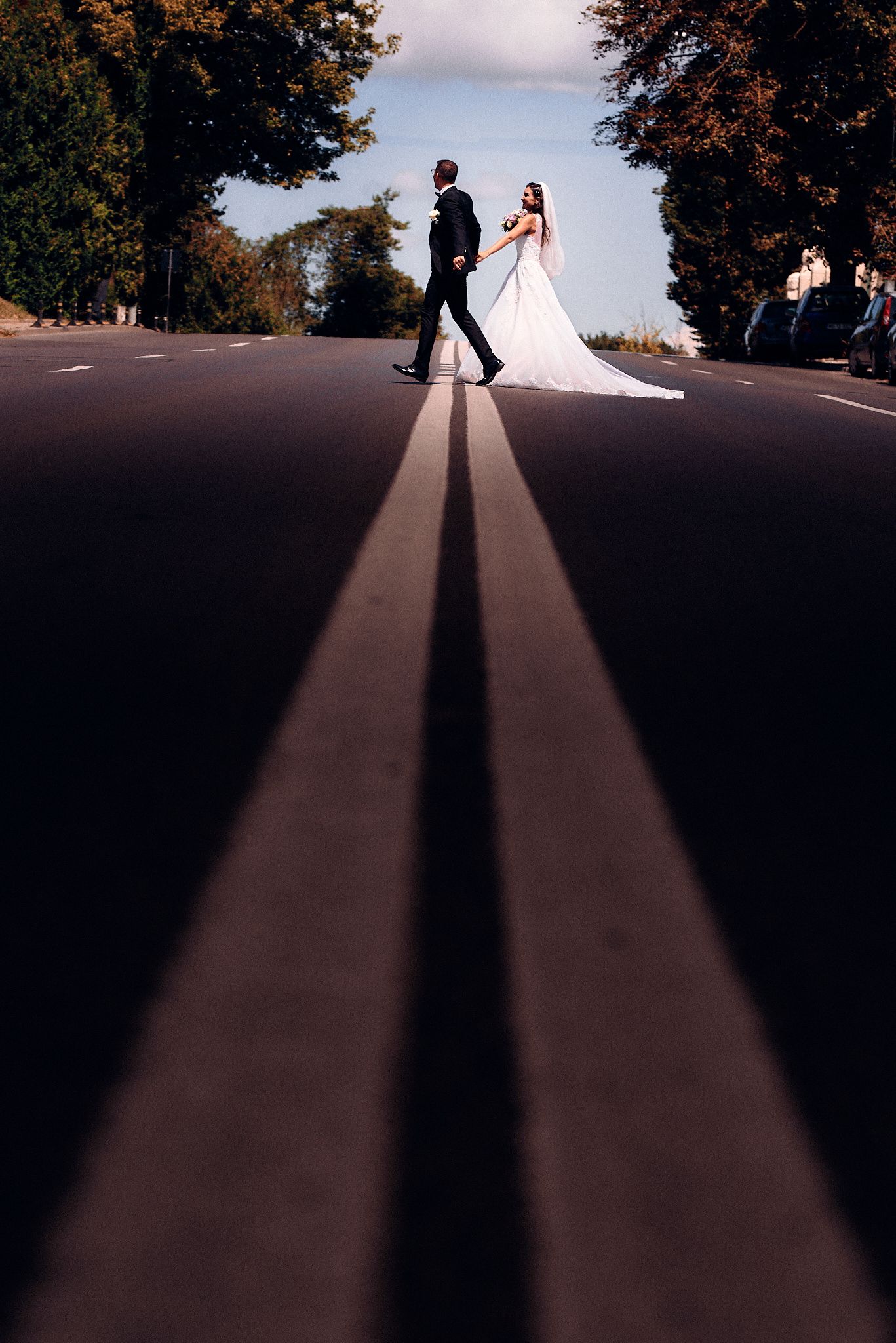 Creative wedding photo with couple walking on road with dramatic leading lines and shadows.
