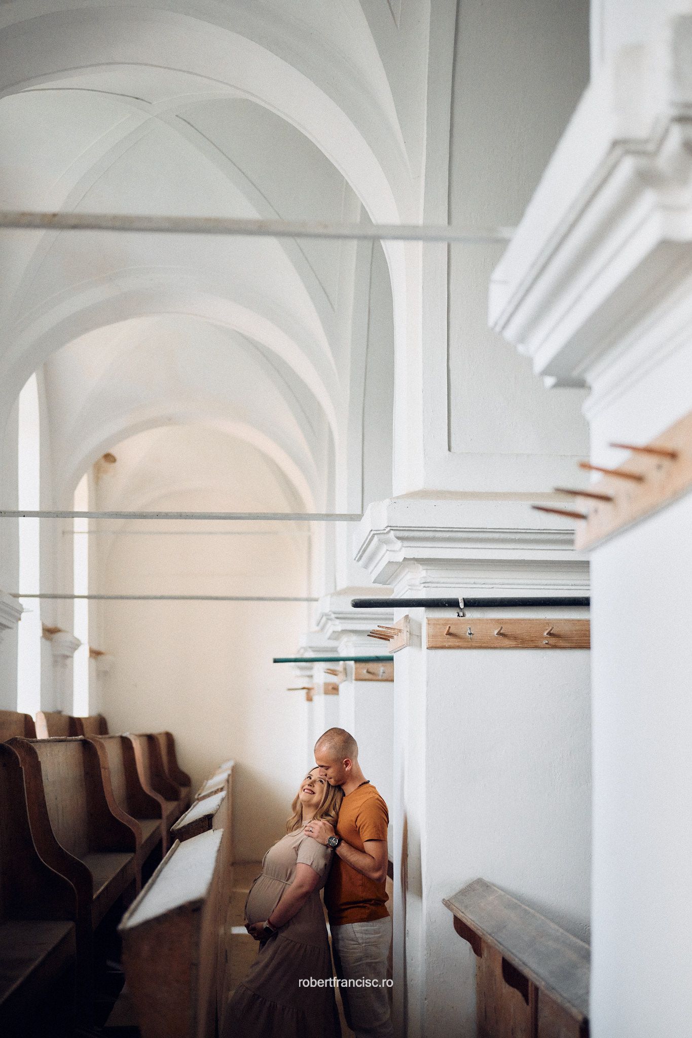 Five connected white arched ceiling rooms in a monastery or church with wooden pews arranged in minimalist fashion.