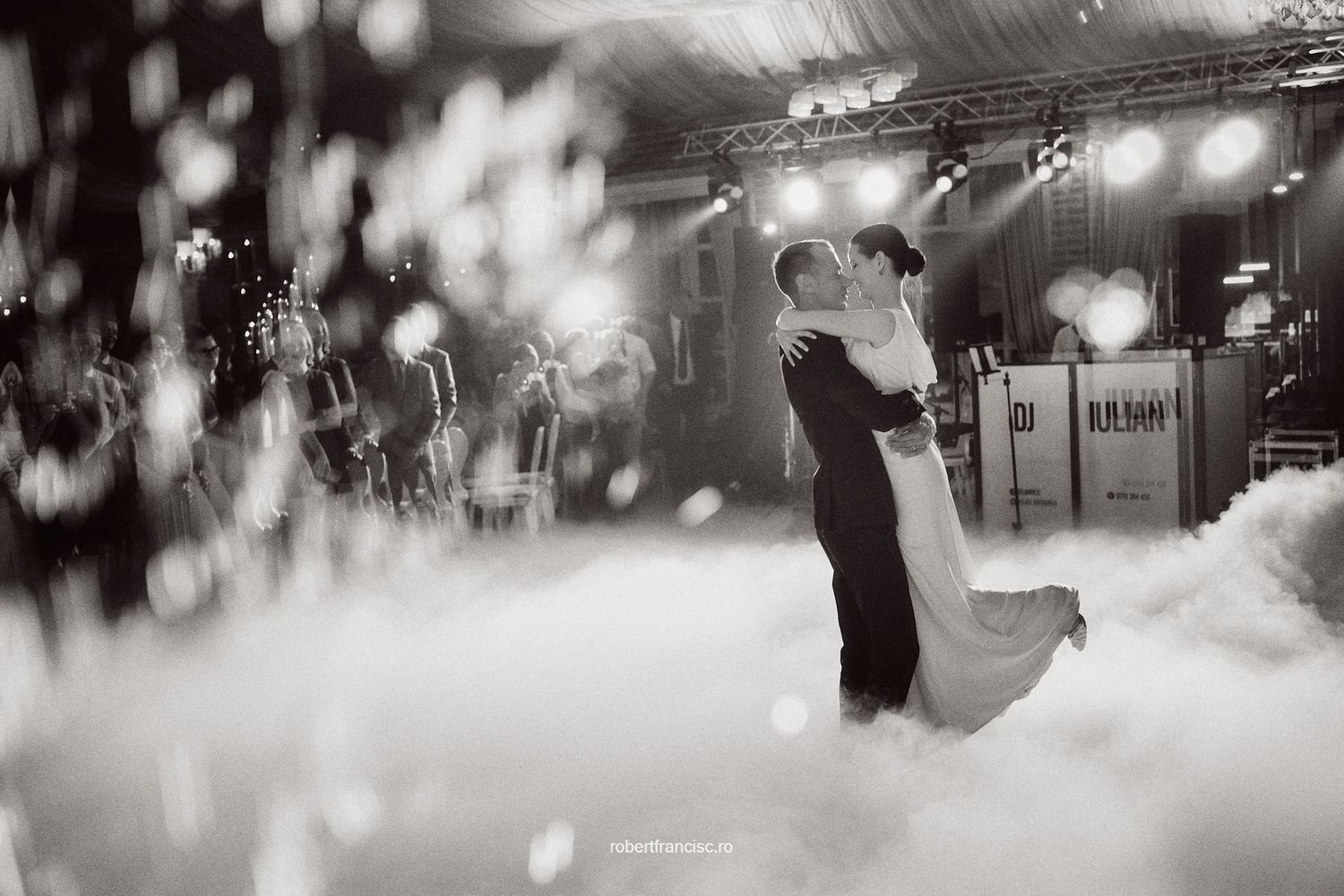 A romantic black and white wedding first dance photo with soft bokeh and dramatic stage lighting creates a dreamy atmosphere.