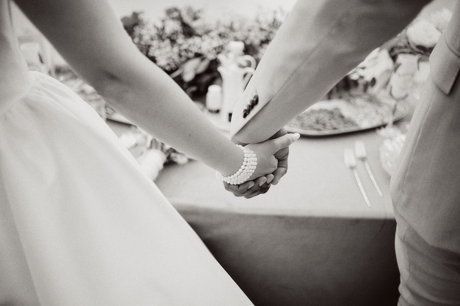 Black and white detail shot of hands during wedding cake cutting ceremony.