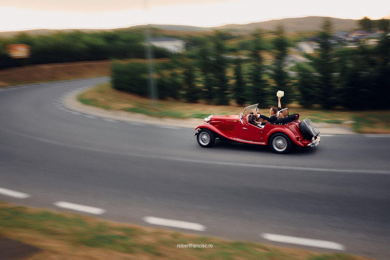 A red vintage sports car drives along a winding mountain road during a scenic mountain journey.