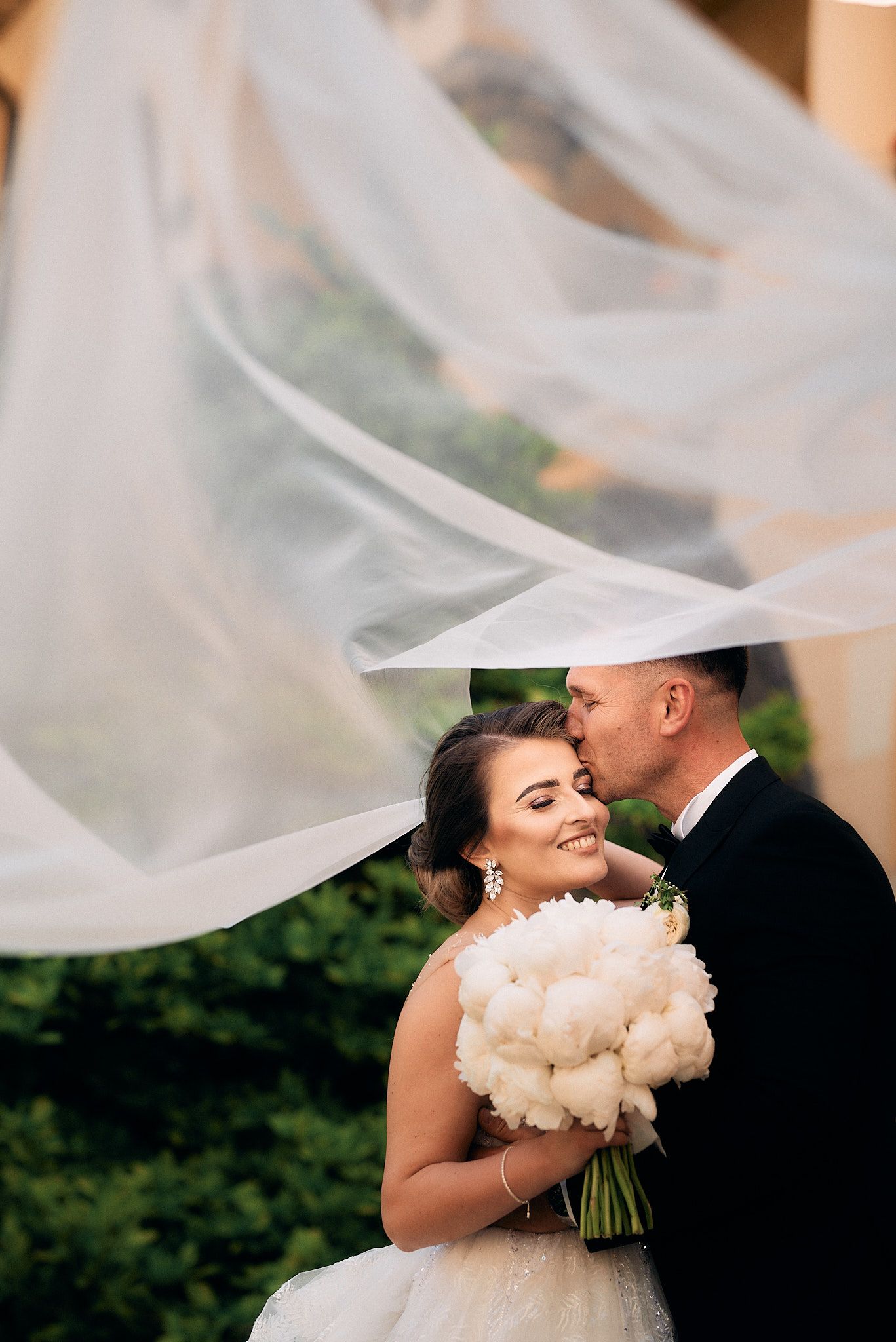 A romantic wedding portrait with flowing veil and white peony bouquet.
