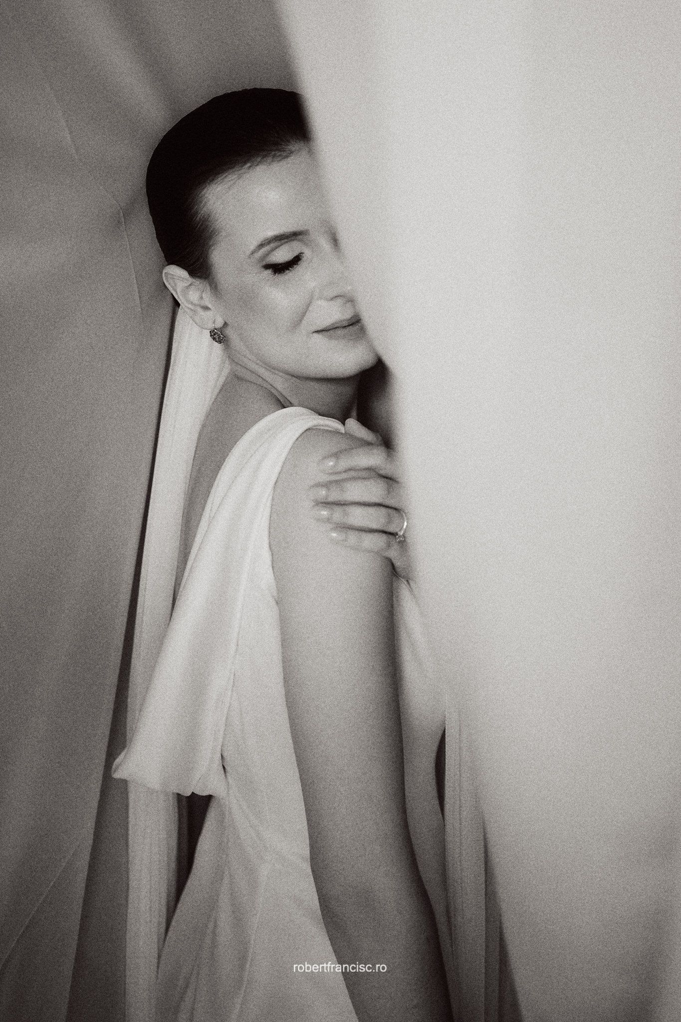 Black and white portrait photograph showing an elegant figure in white fabric with closed eyes in a contemplative pose.