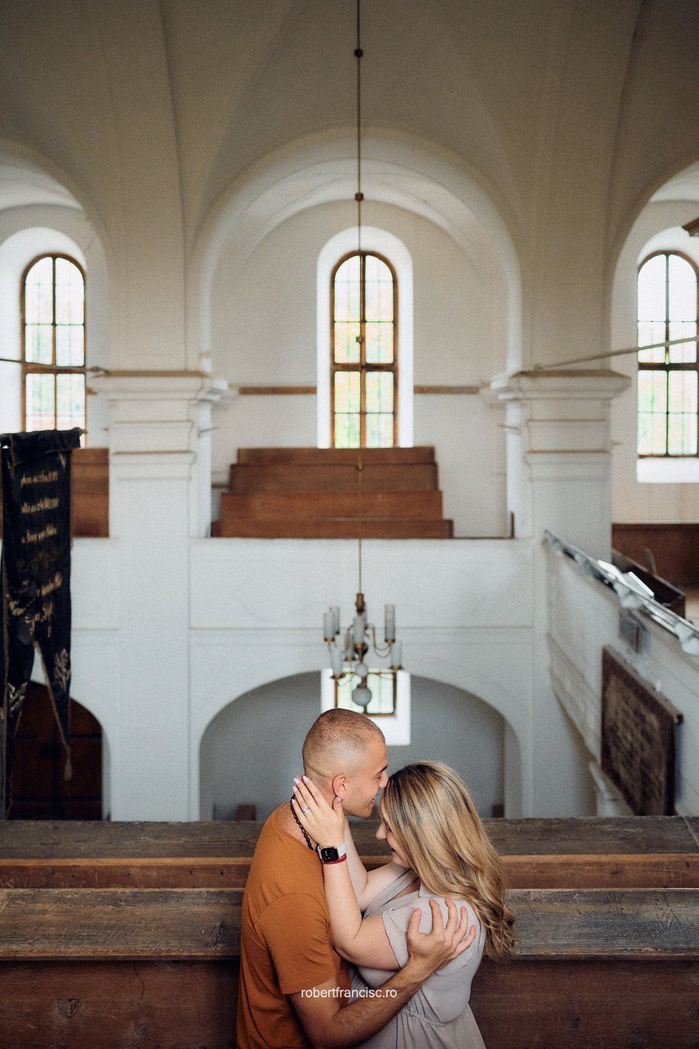 A romantic moment shared between a couple in a historic church interior with arched windows and wooden pews.