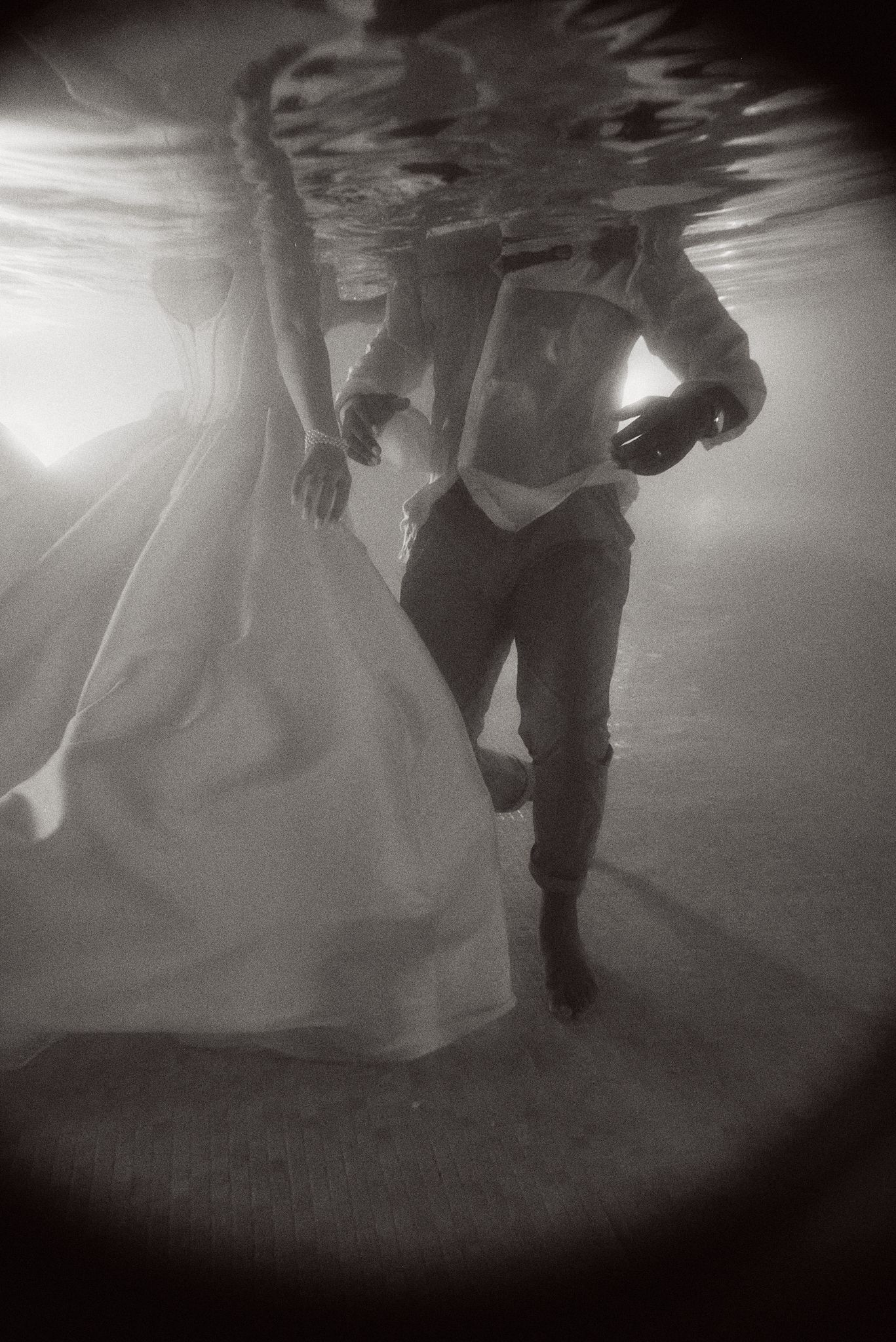 Artistic underwater black and white portrait of couple in wedding attire.