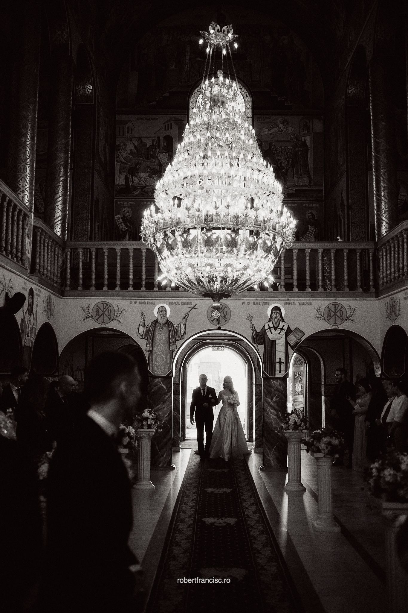 Silhouetted figures dance beneath ornate crystal chandeliers in a grand ballroom during an elegant reception.