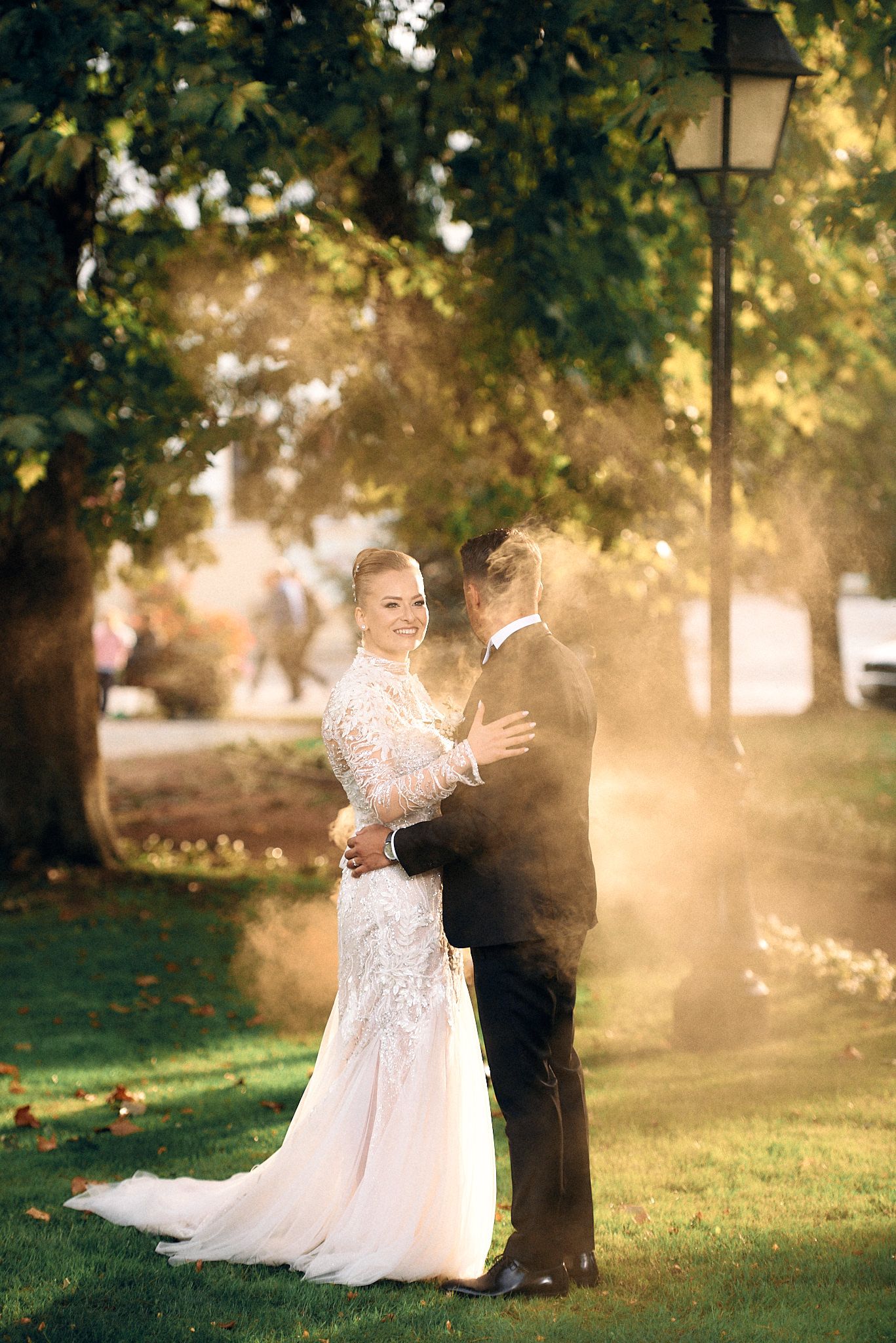 Ethereal wedding portrait in sunset-lit park with glowing golden light filtering through trees.