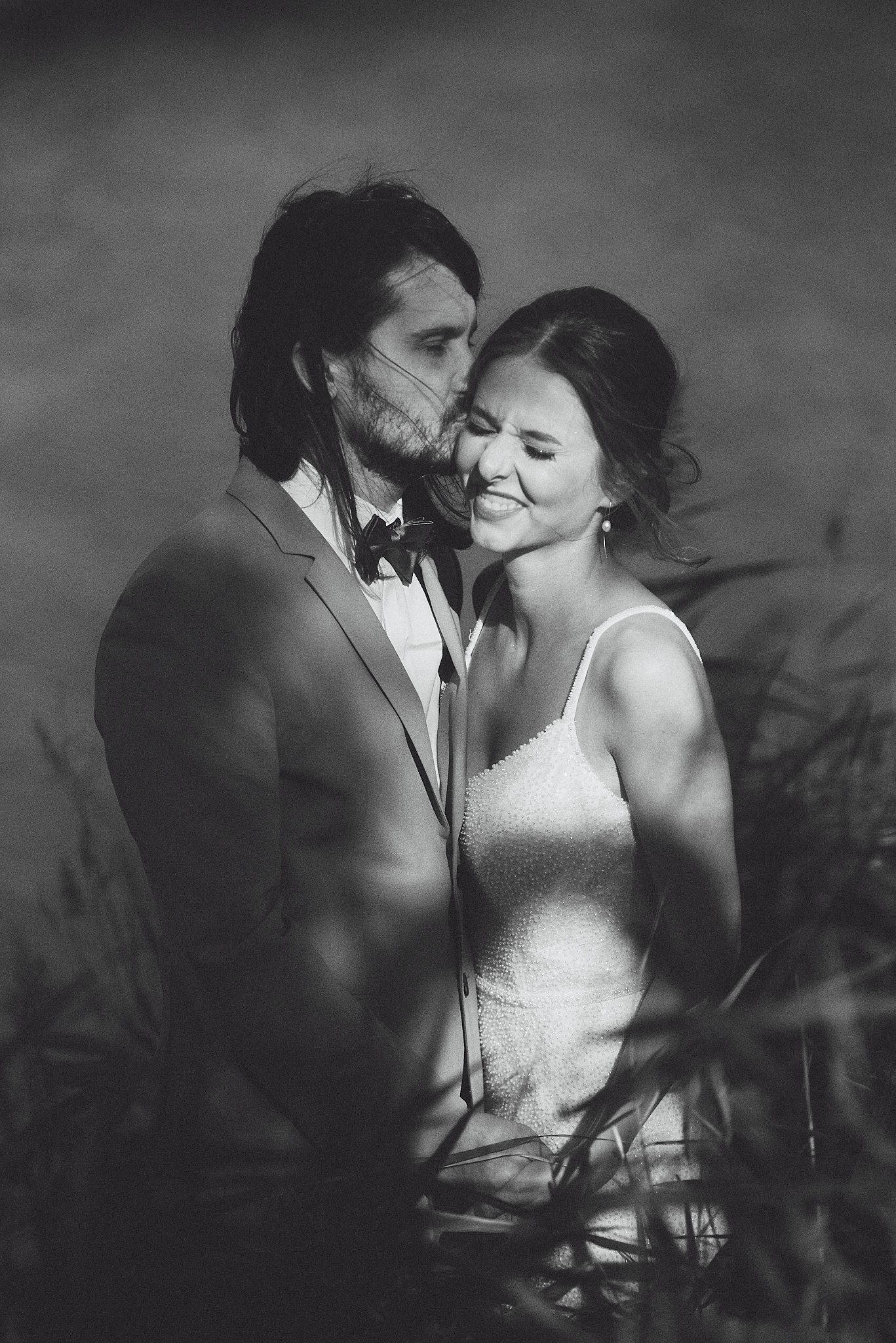 Intimate black and white wedding portrait showing tender moment between couple in formal attire.