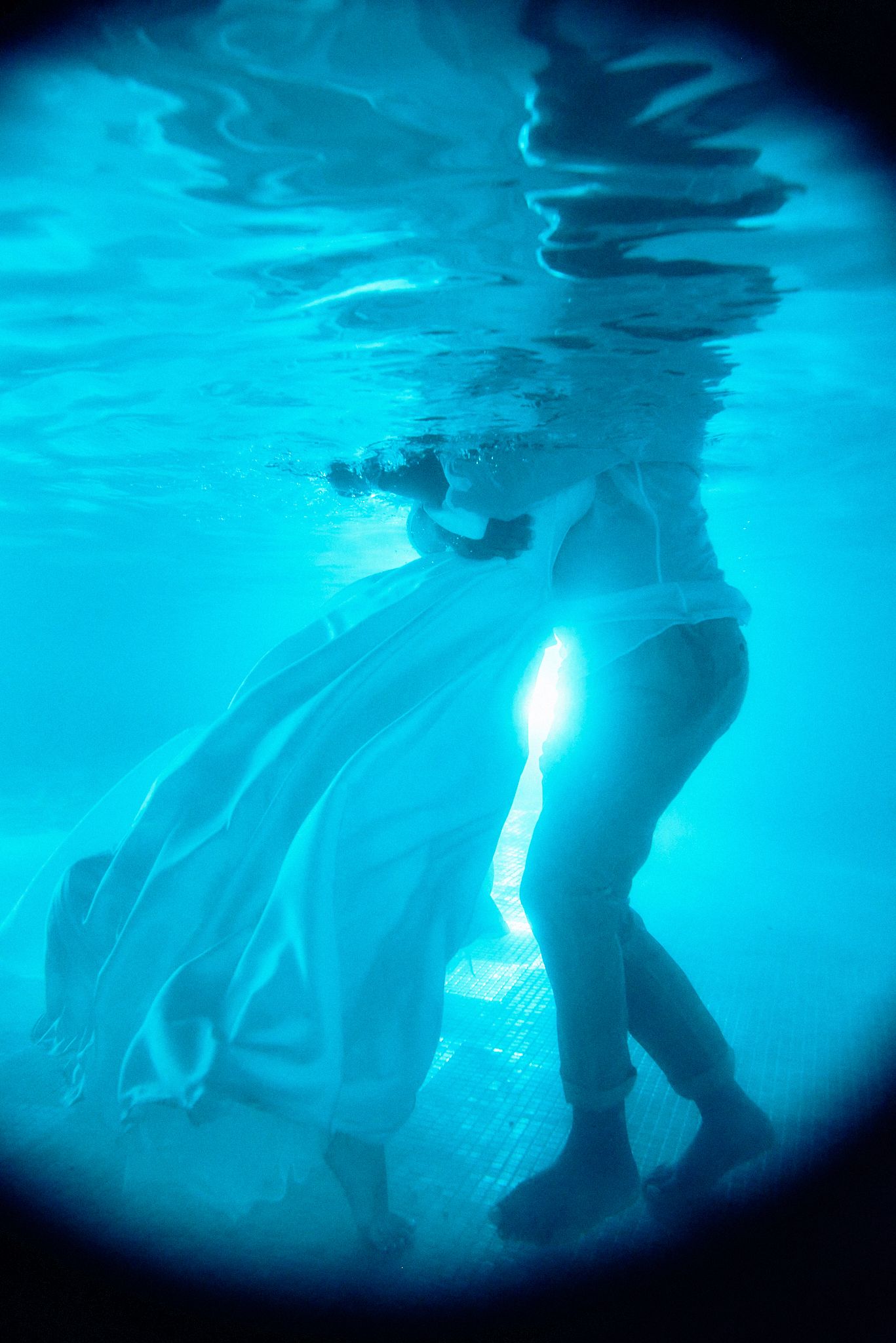 Underwater photo of flowing white dress creating ethereal effect in blue water.