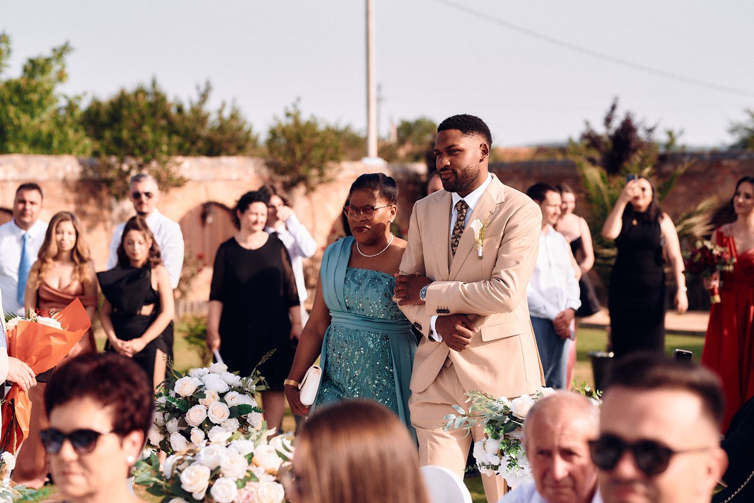 Outdoor wedding ceremony with guests seated on chairs and floral decorations.